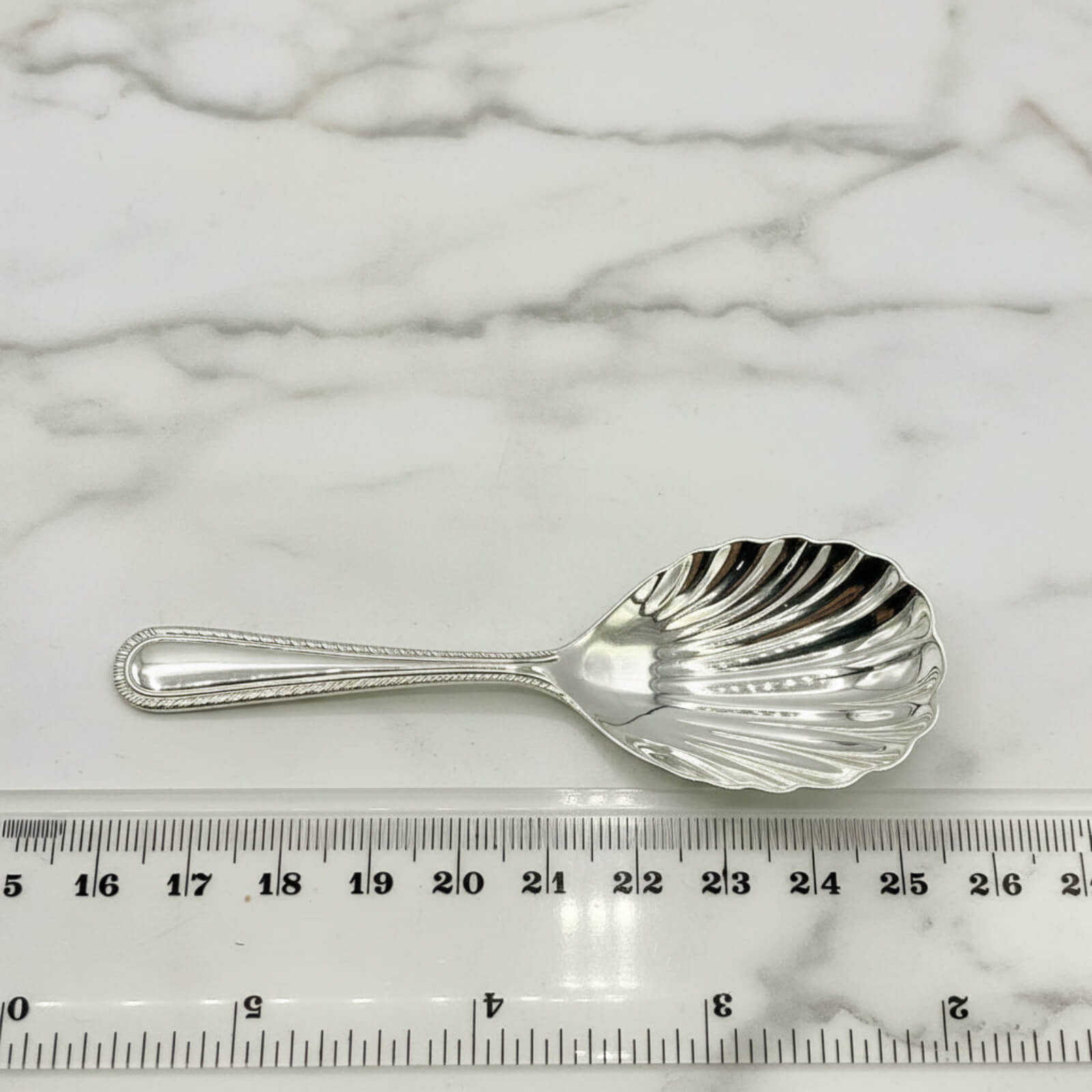 Vintage 1977 Sterling Silver Tea Caddy Spoon next to a tape measure on a marble background