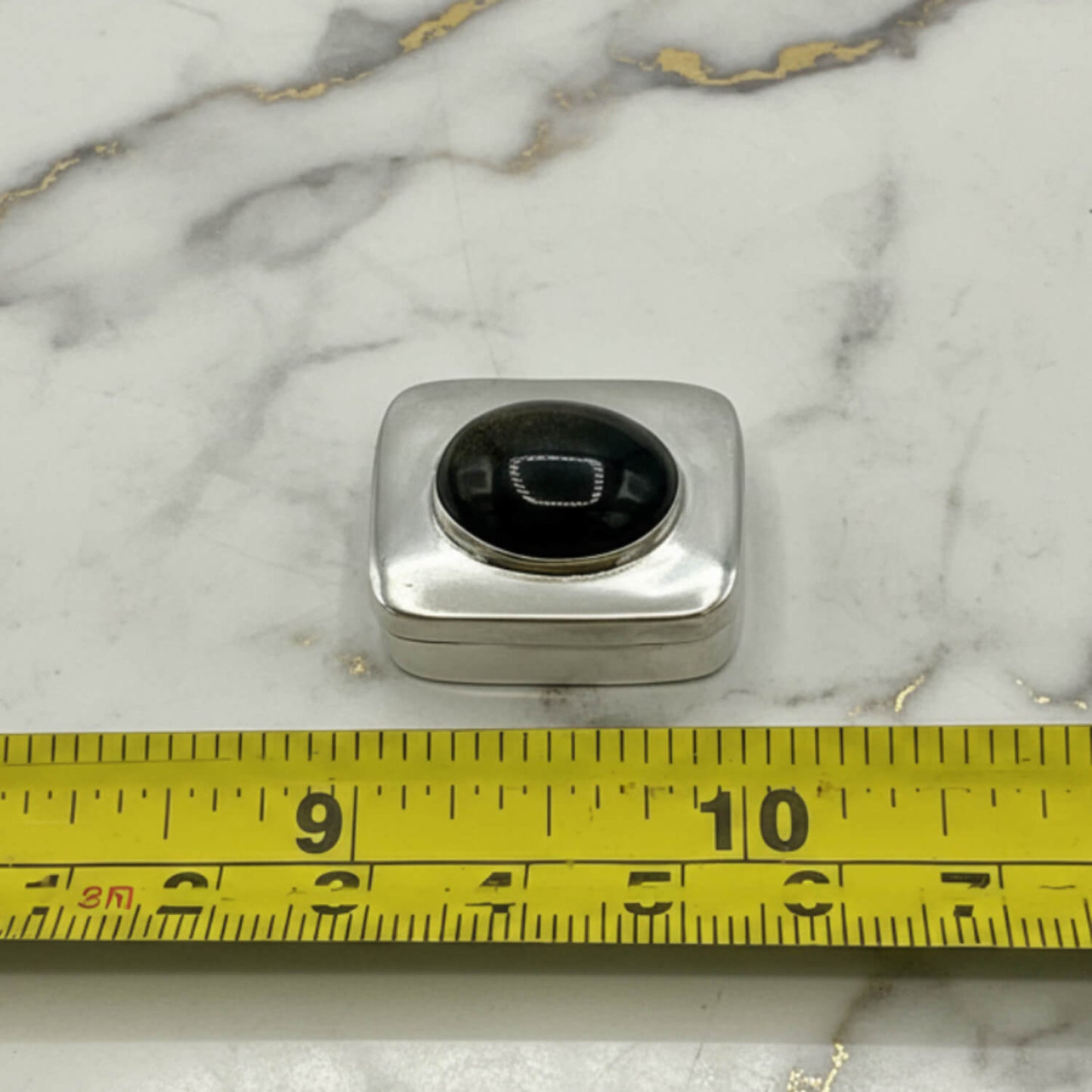 Vintage Black Gemstone Silver Pill Box next to a tape measure for scale on marble