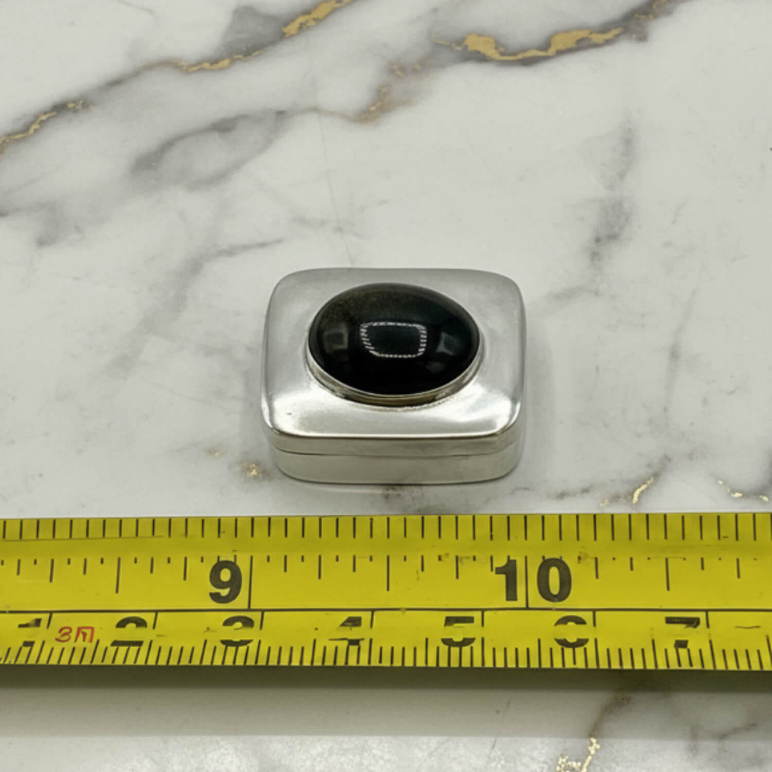 Vintage Black Gemstone Silver Pill Box next to a tape measure for scale on marble