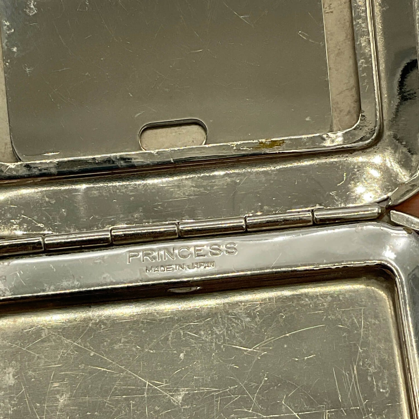 Close-up of an open silver-toned Princess compact case with a mirror in the lid and the brand name engraved on the hinge.