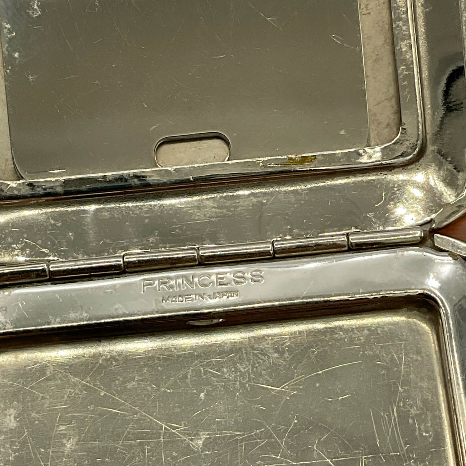 Close-up of an open silver-toned Princess compact case with a mirror in the lid and the brand name engraved on the hinge.