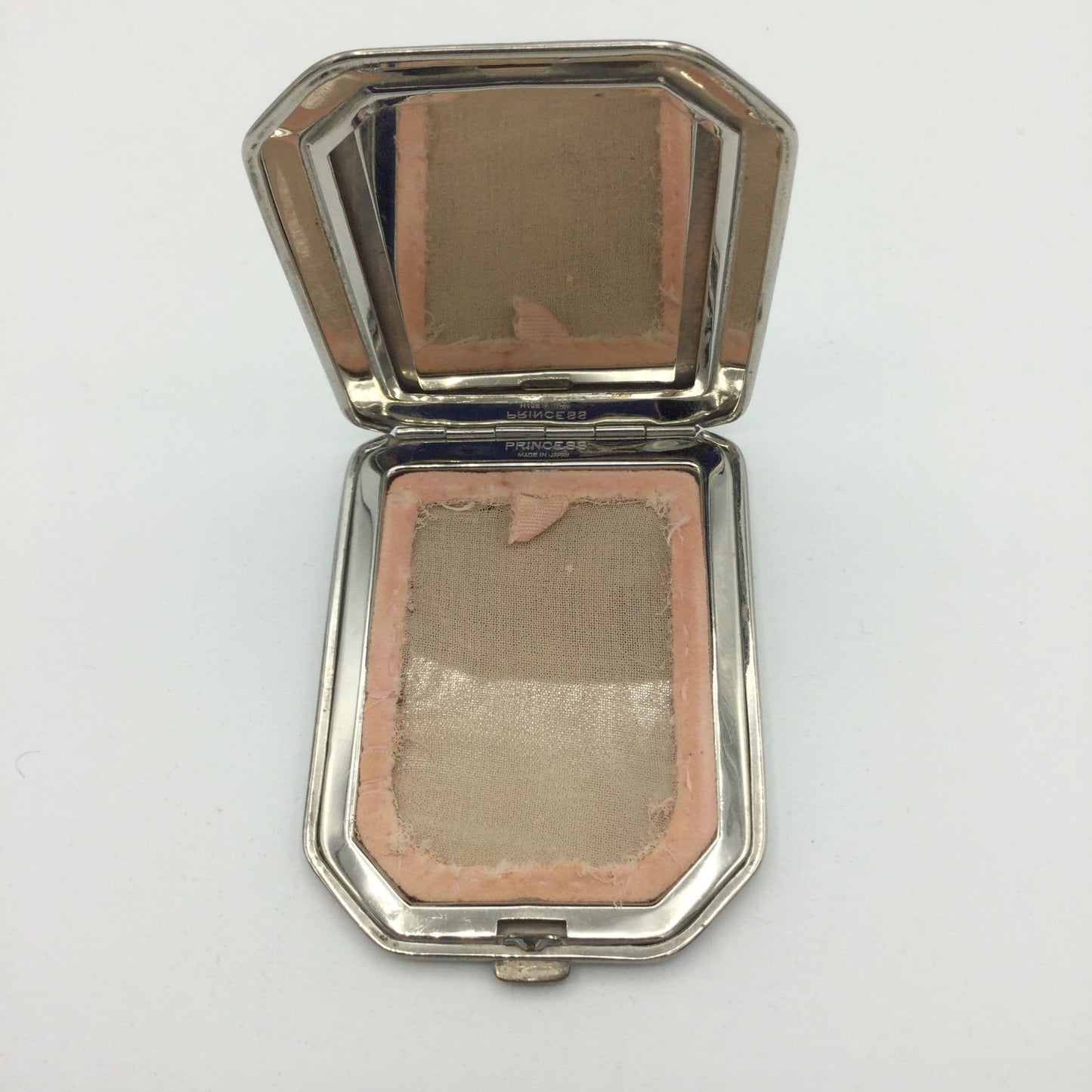 An open vintage octagonal silver compact containing a pressed powder blush screen with a dusty rose color, set against a plain white background.