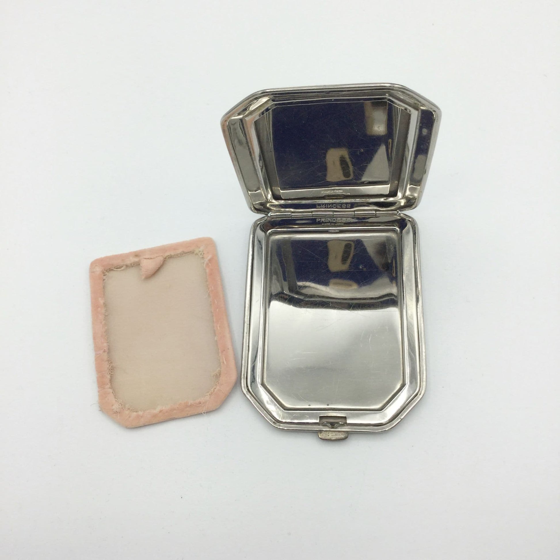 A vintage octagonal silver-toned metal compact case shown open, with its pink fabric lining and backing cover placed beside it on a plain white background.
