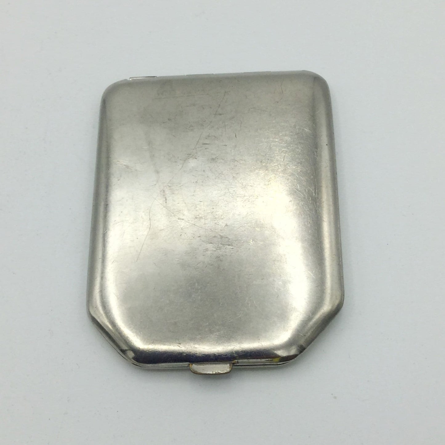 A vintage silver-toned metal powder compact with a rounded rectangular shape and a small hinge at the bottom, shown on a plain light background.