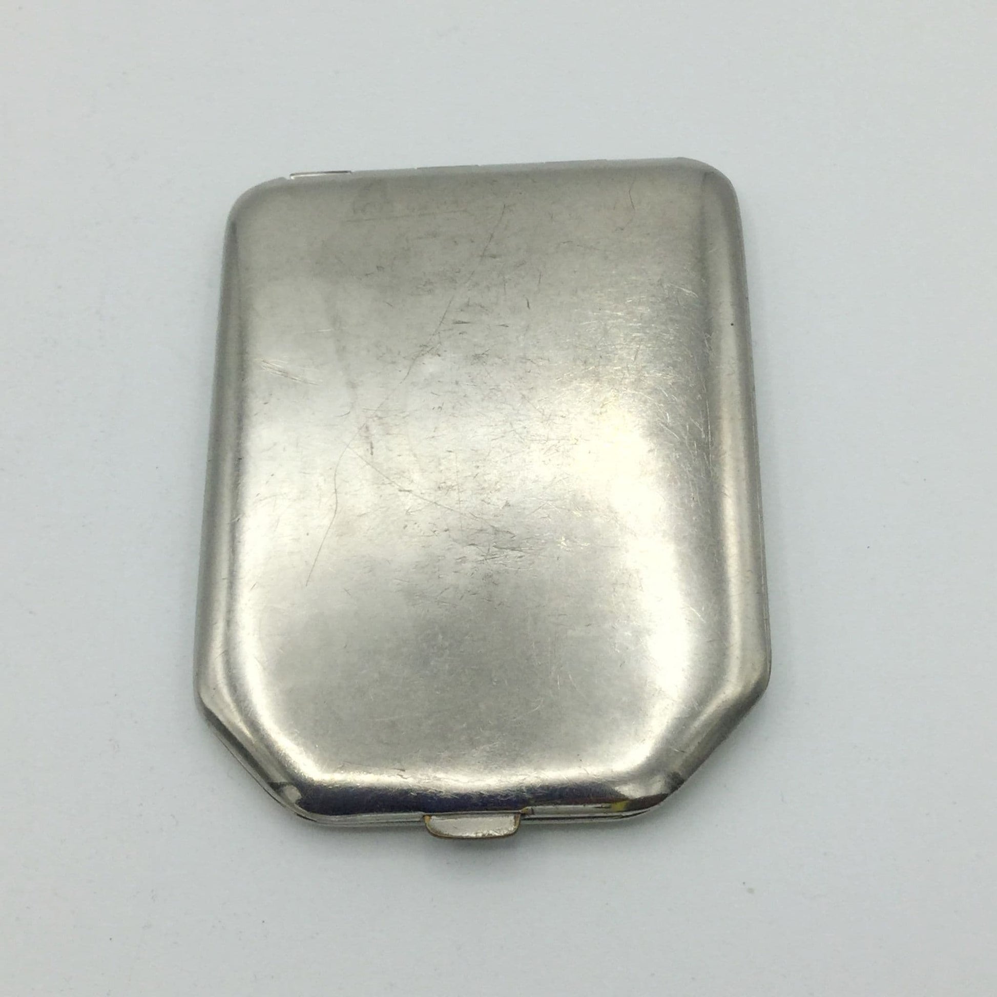 A vintage silver-toned metal powder compact with a rounded rectangular shape and a small hinge at the bottom, shown on a plain light background.