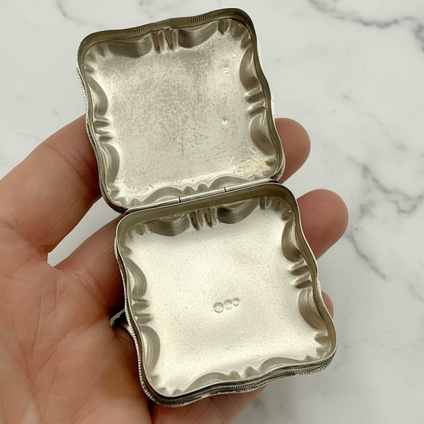 Vintage Small Dutch Silver Box Open showing the inside held in fingers with a marble background 