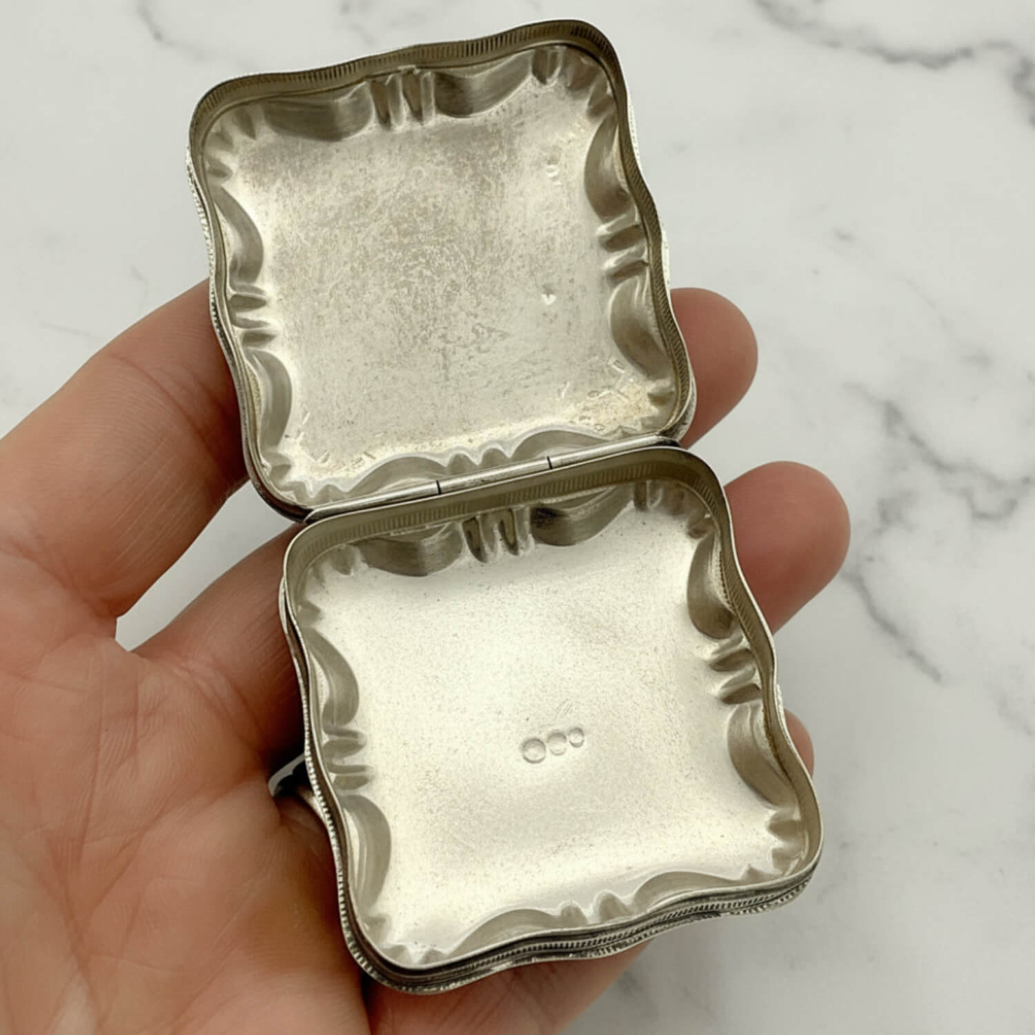 Vintage Small Dutch Silver Box Open showing the inside held in fingers with a marble background 