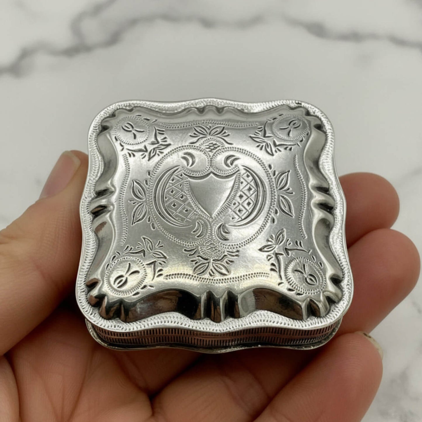Vintage Small Dutch Silver Box Lid held in fingers with a marble background 