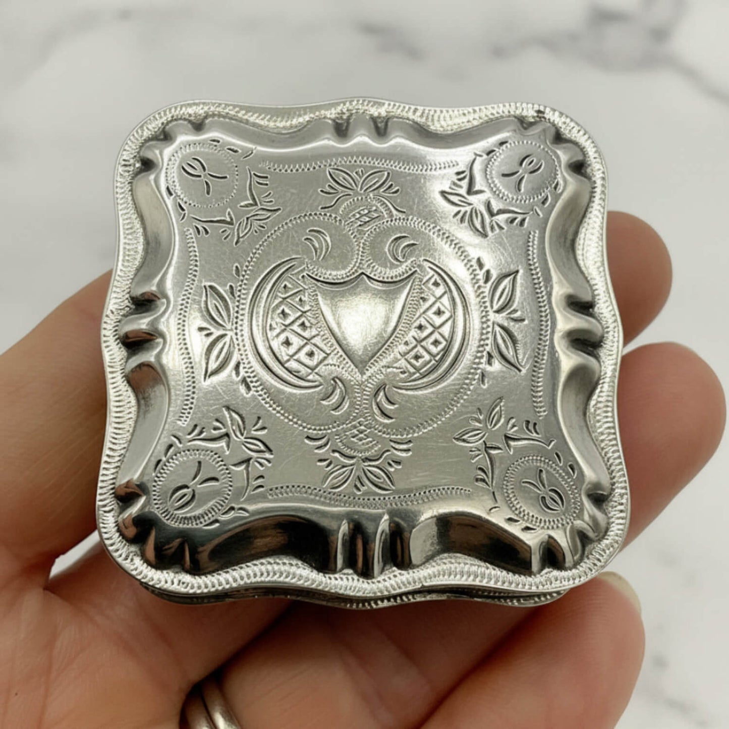 Vintage Small Dutch Silver Box Lid held in fingers with a marble background 
