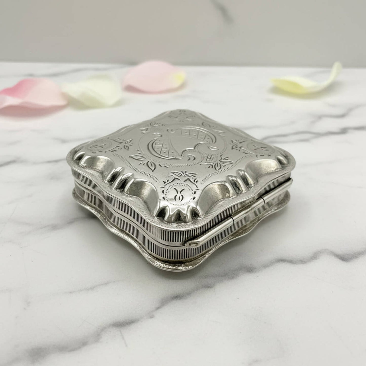 Vintage Small Dutch Silver Box On a marble surface with petals in the background 