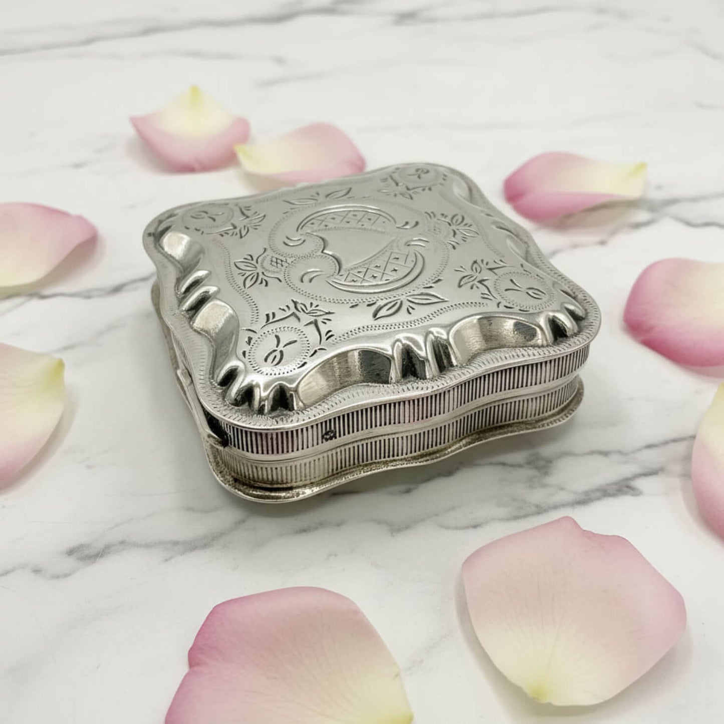 Vintage Small Dutch Silver Box On a marble surface surrounded by petals