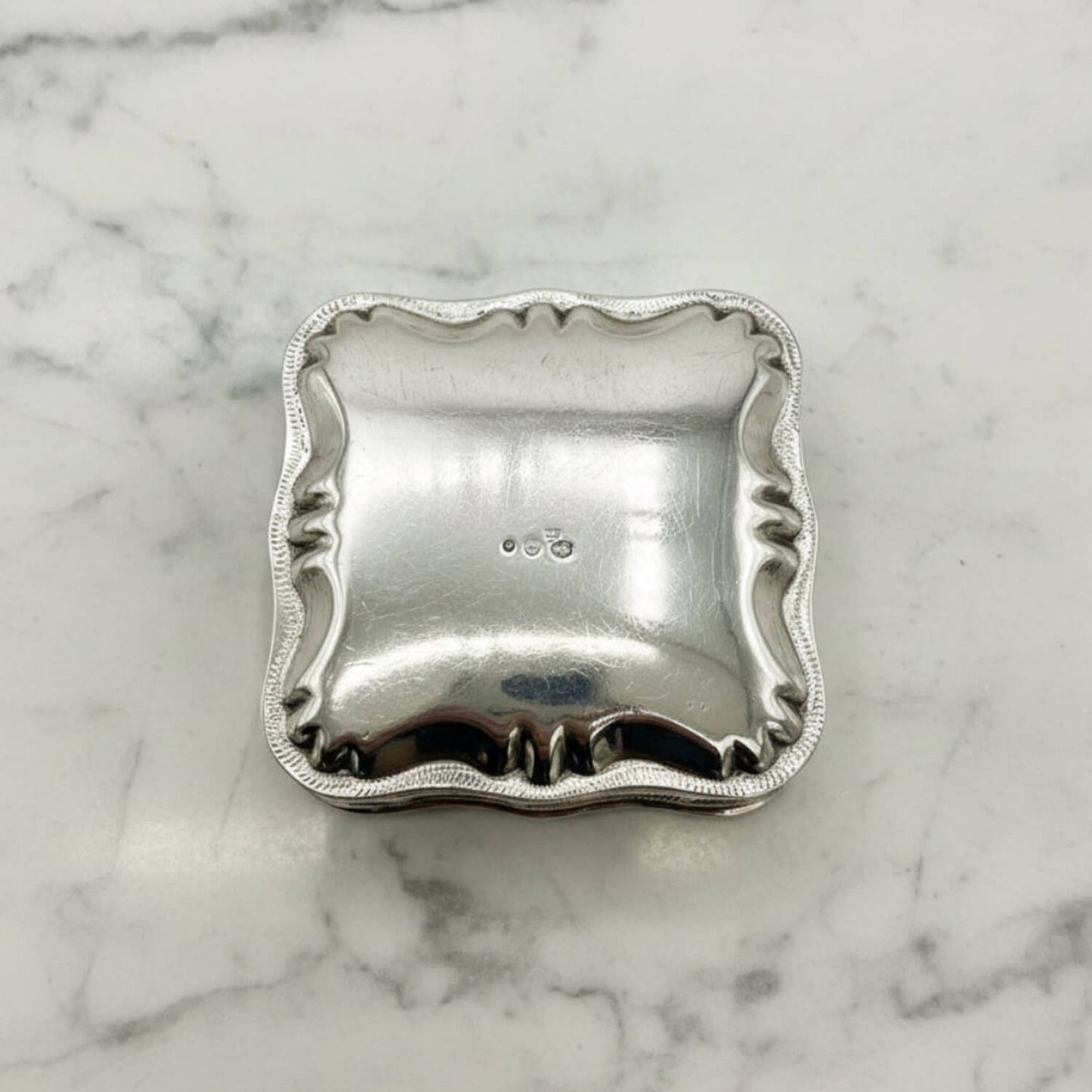 Vintage Small Dutch Silver Box Upside down showing hallmarks on the base on a marble surface 
