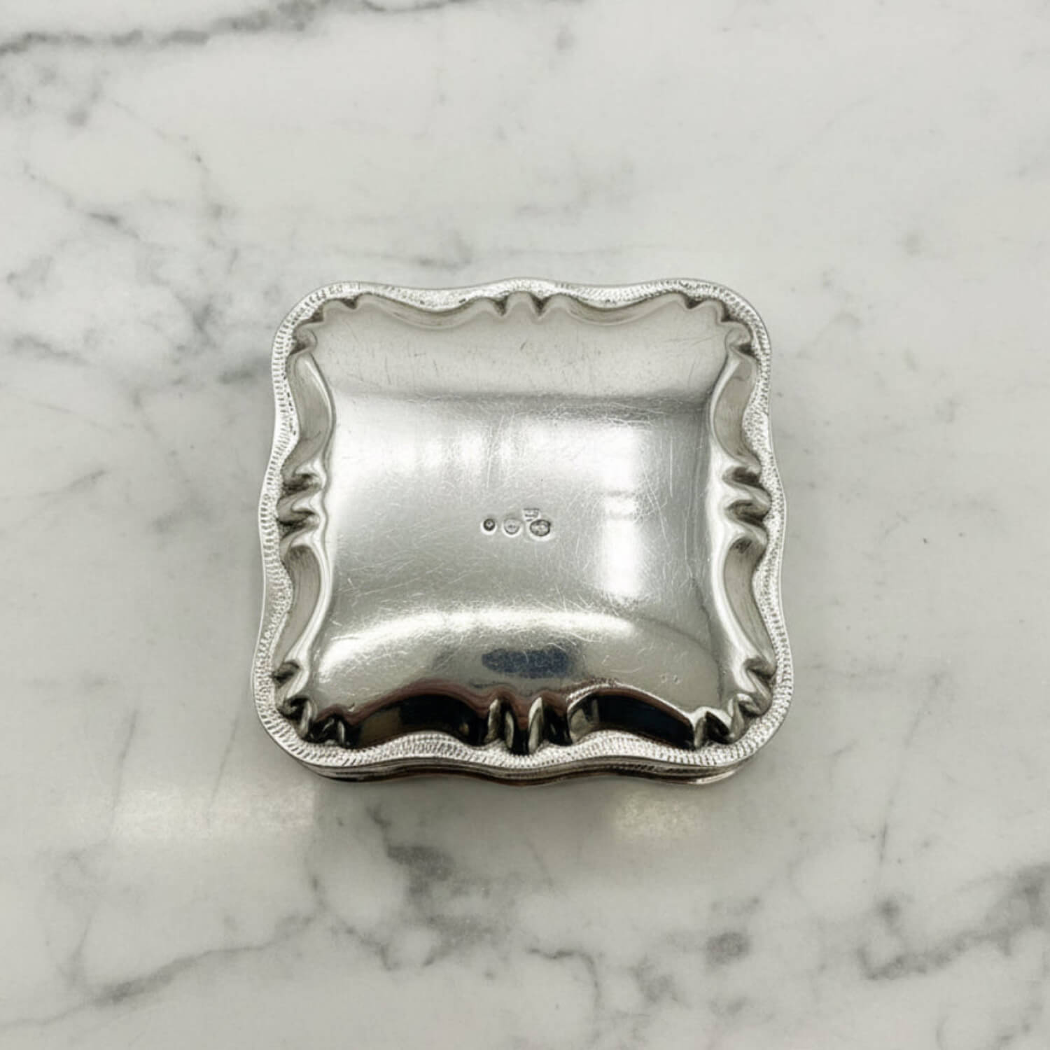 Vintage Small Dutch Silver Box Upside down showing hallmarks on the base on a marble surface 