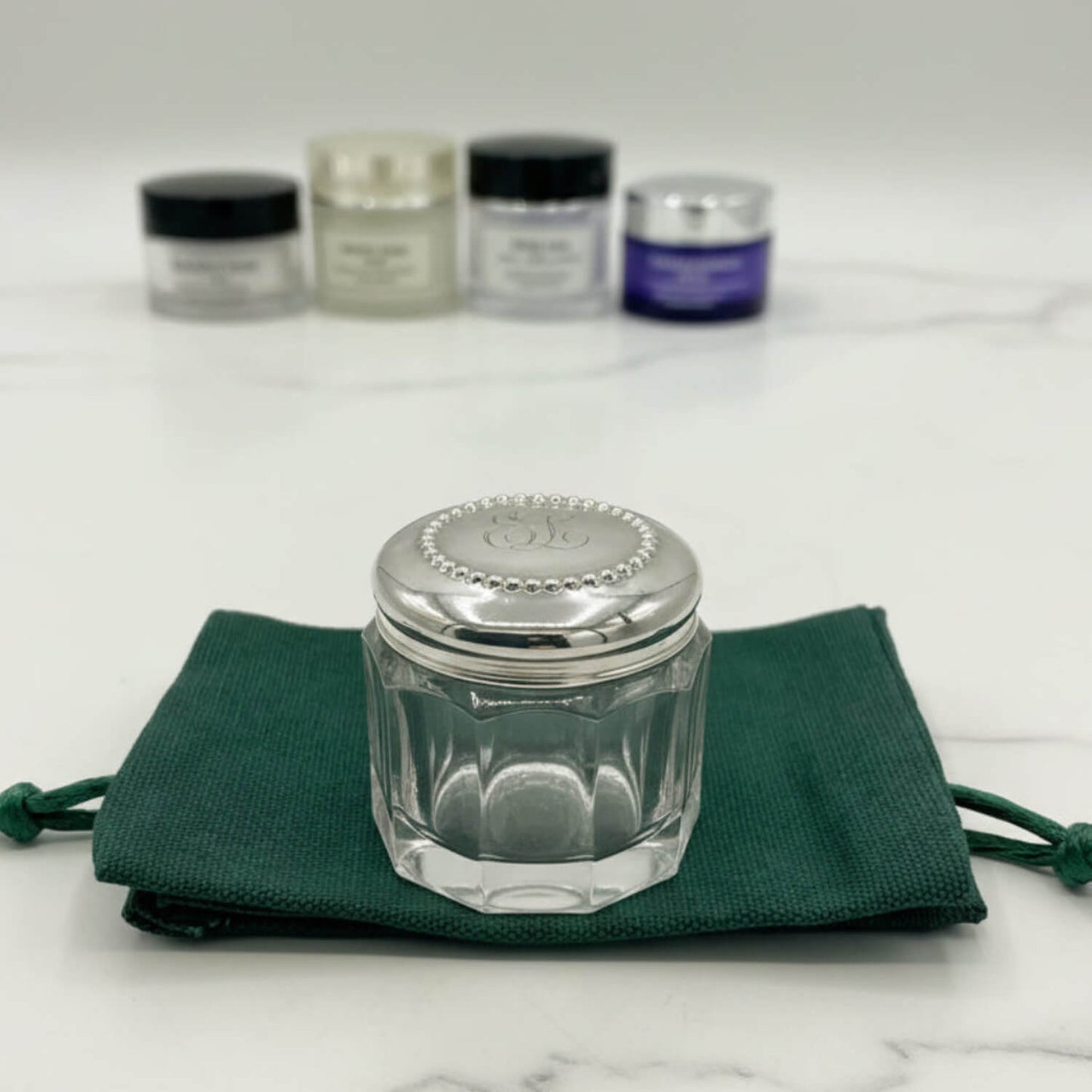 Clear glass jar with silver lid on a green cloth, with other similar jars in the background.