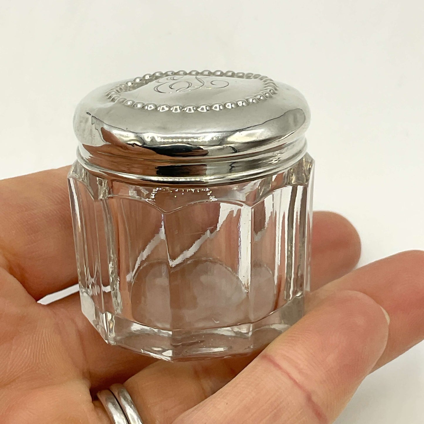 Clear glass jar with silver lid held in a hand against a white background