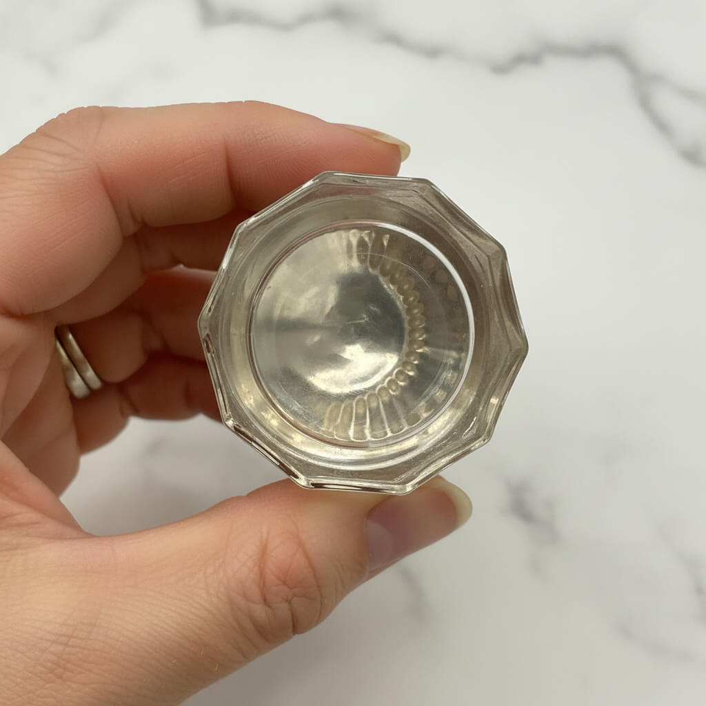 Hand holding a small silver jar against a marble background