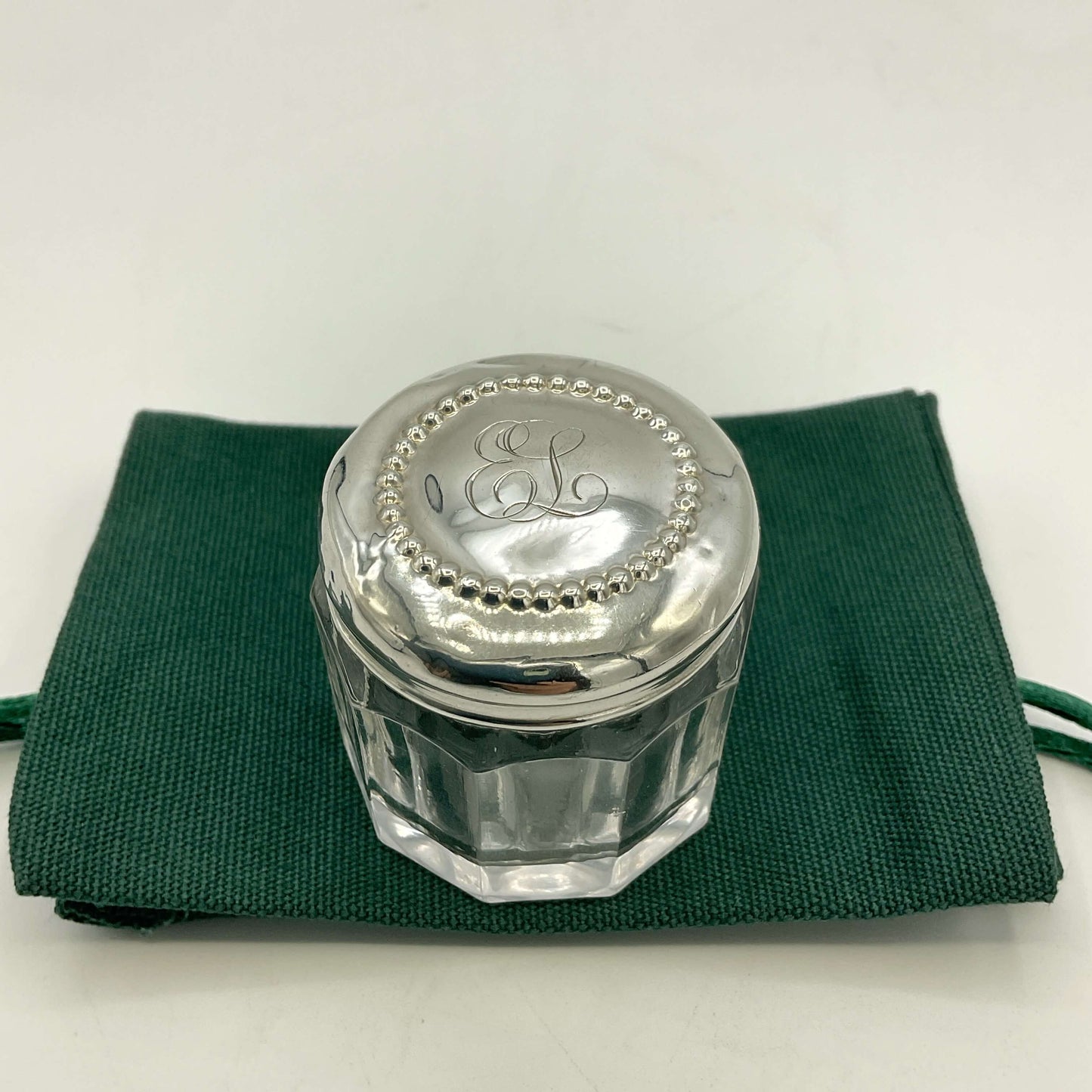 Silver lid with 'EL' initials on a glass container, placed on a green cloth.