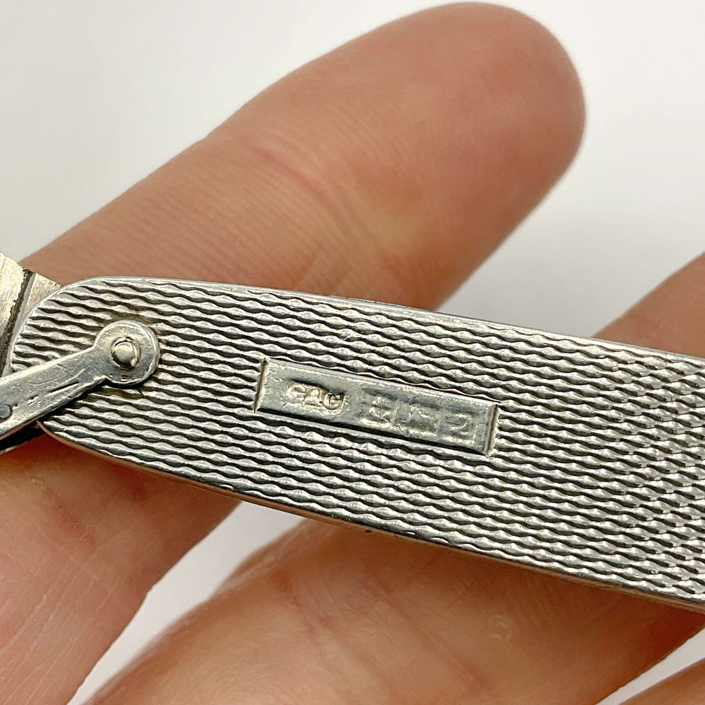 Close-up of a silver pen knife hallmarks held between fingers with a blurred background