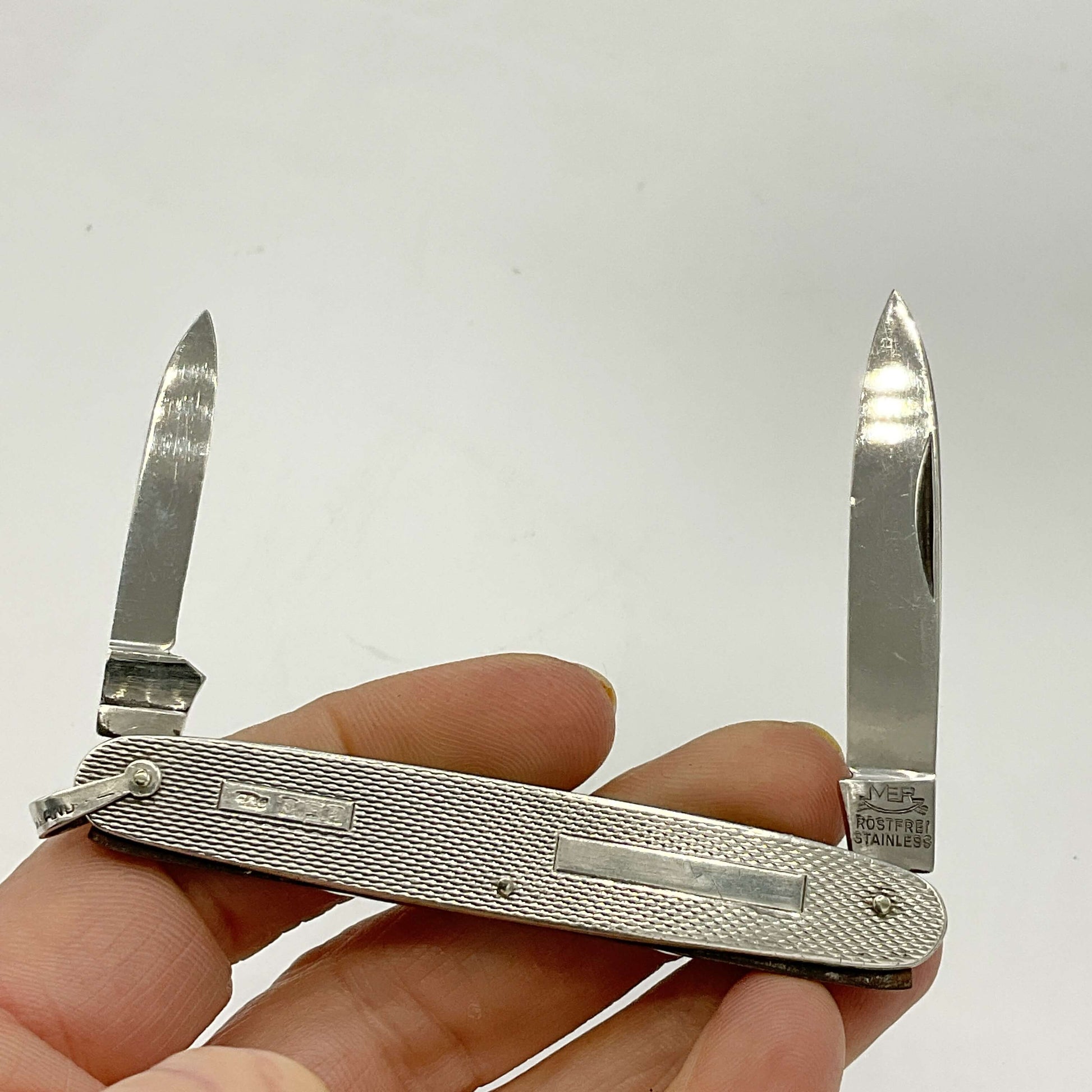 Silver pen knife with two blades open, held by a hand on a white background