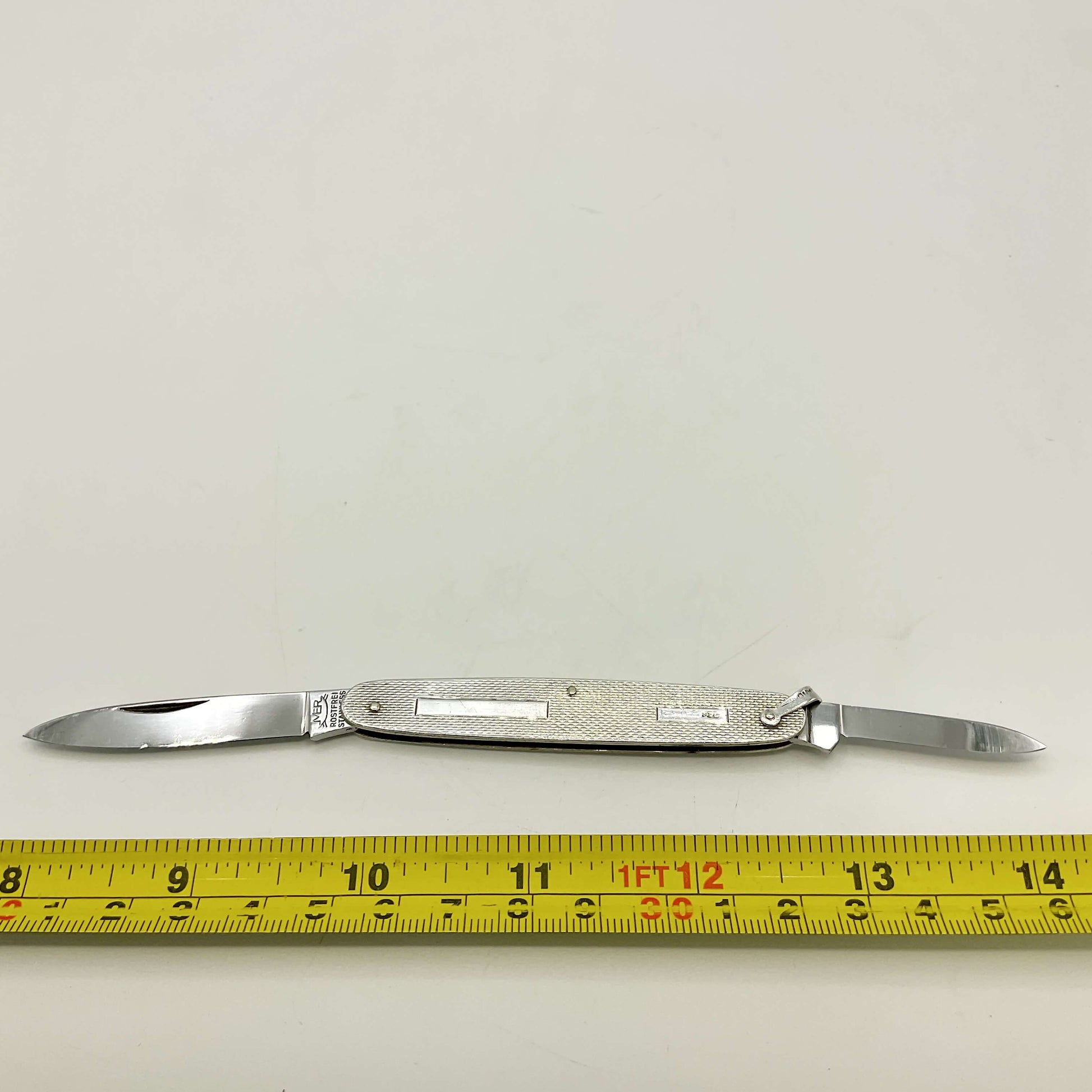 Pen knife with two blades on a white background, measured by a yellow tape measure.
