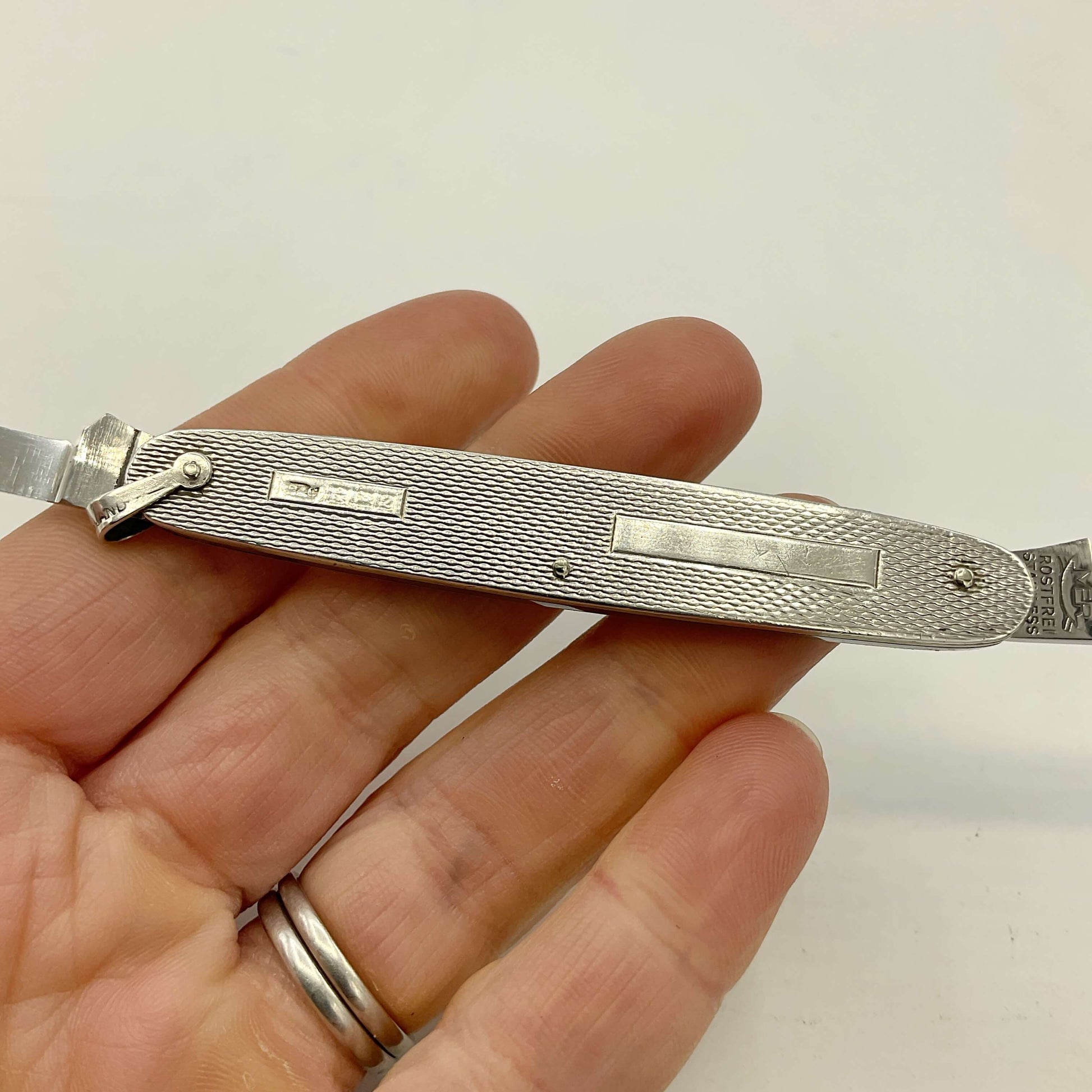 Silver pen knife held in a hand with a plain background