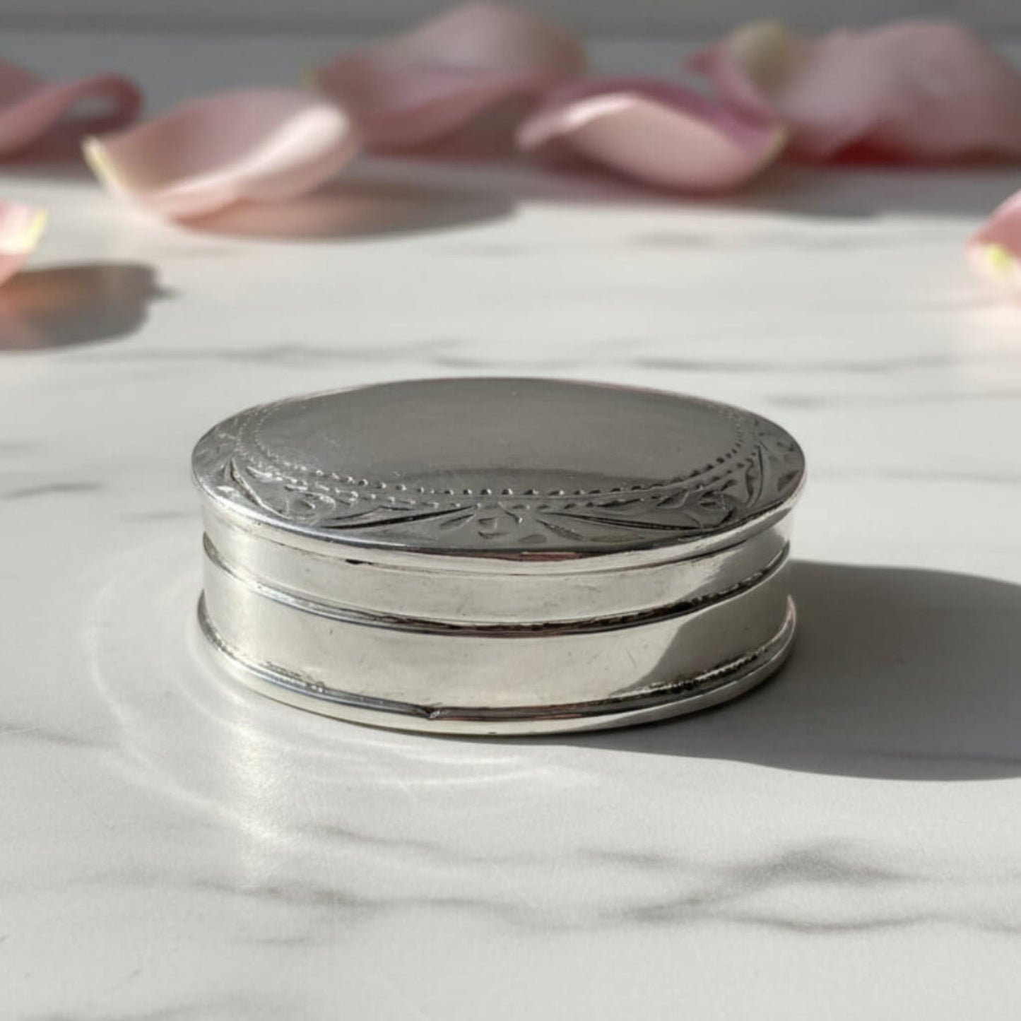 Vintage Sterling Silver Pill Box on a marble surface with petals in the background