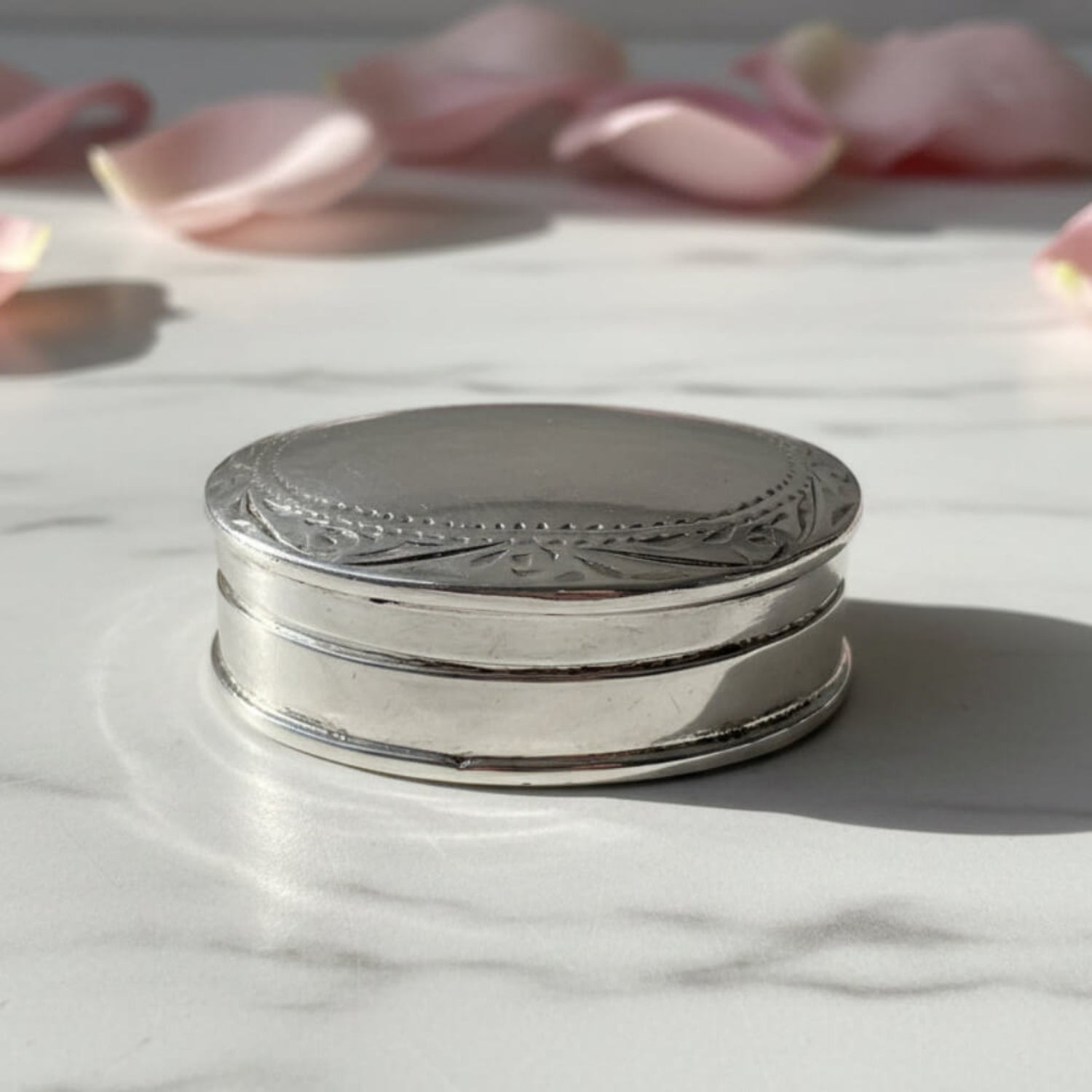 Vintage Sterling Silver Pill Box on a marble surface with petals in the background