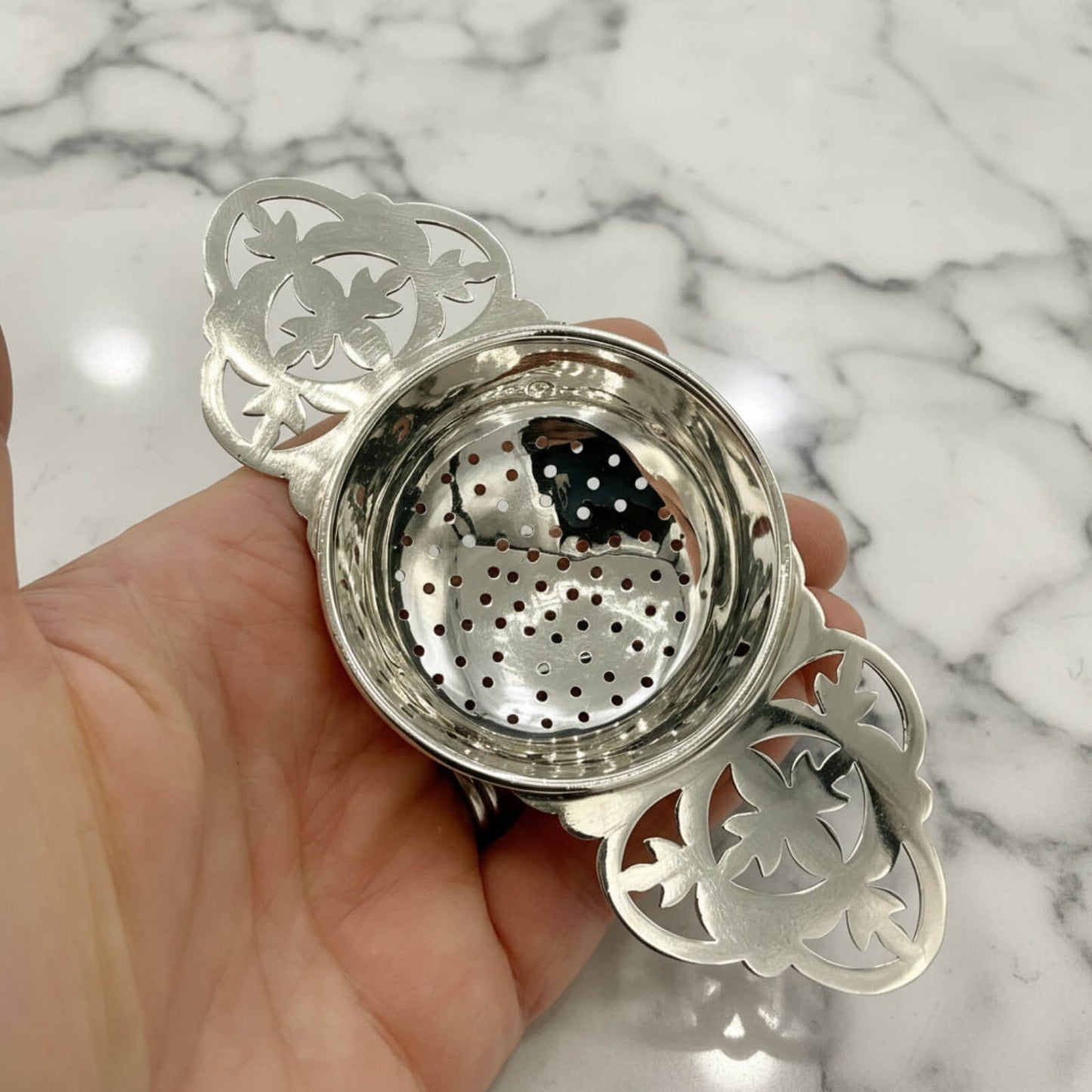 Silver tea infuser held in a hand against a marble background