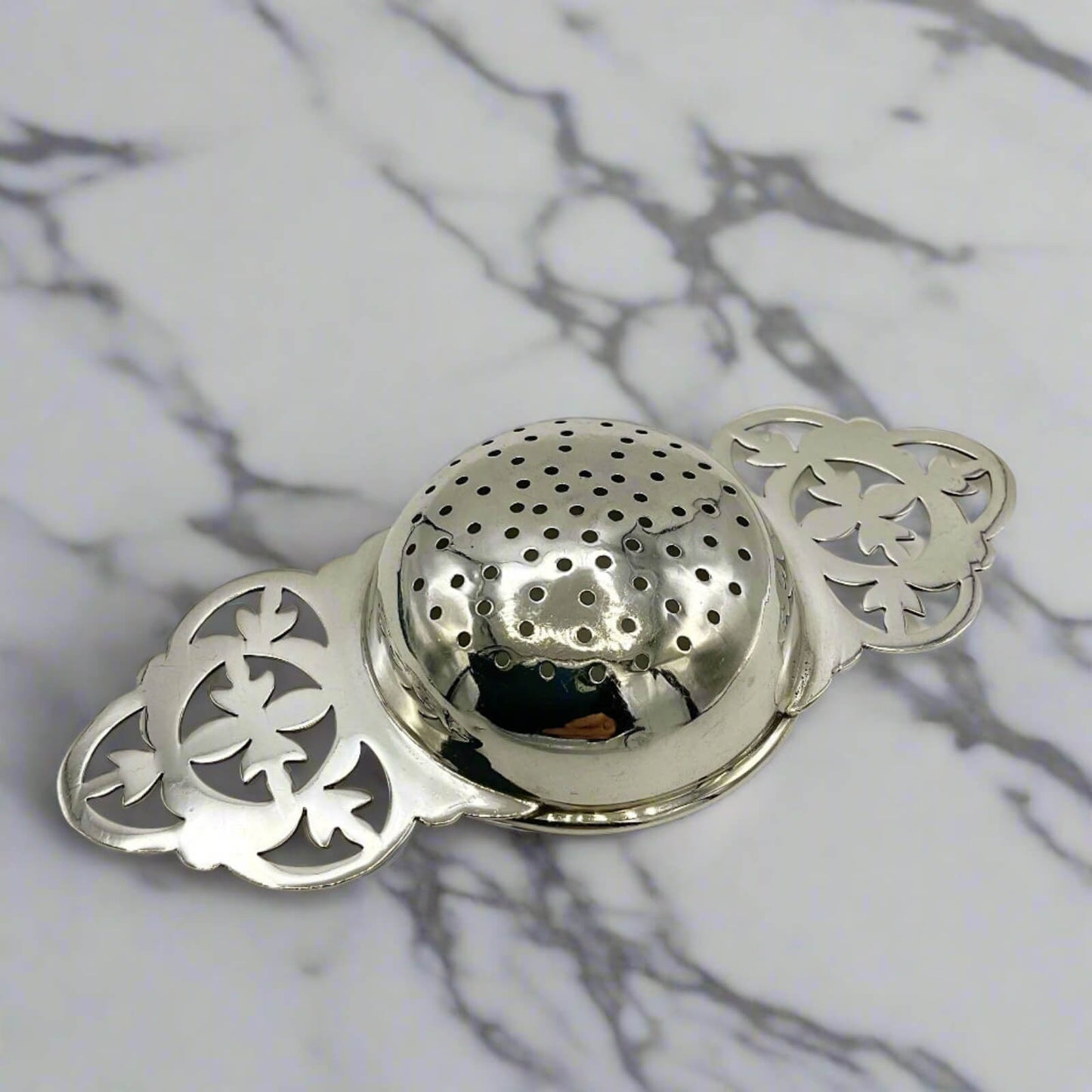 Silver tea infuser with intricate design on a marble background