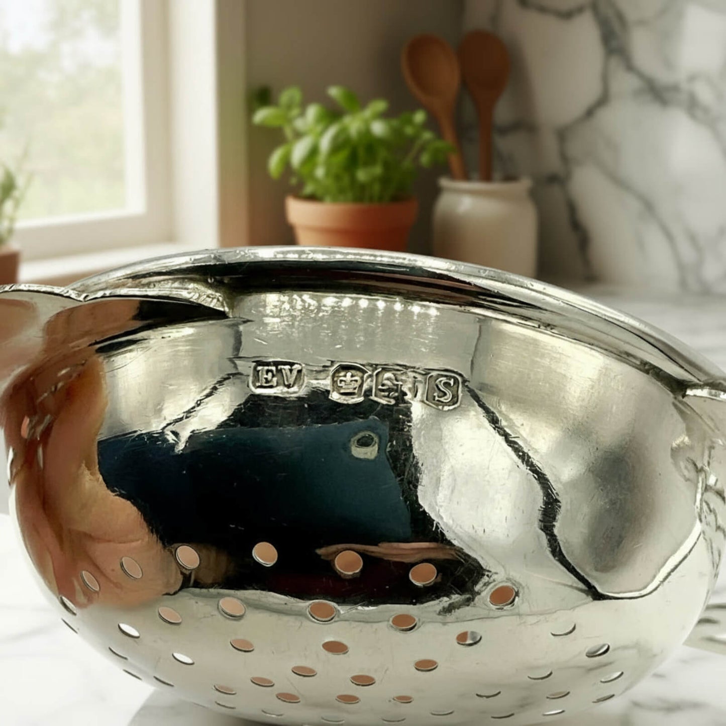Silver tea strainer with 'EV' stamp in a kitchen setting
