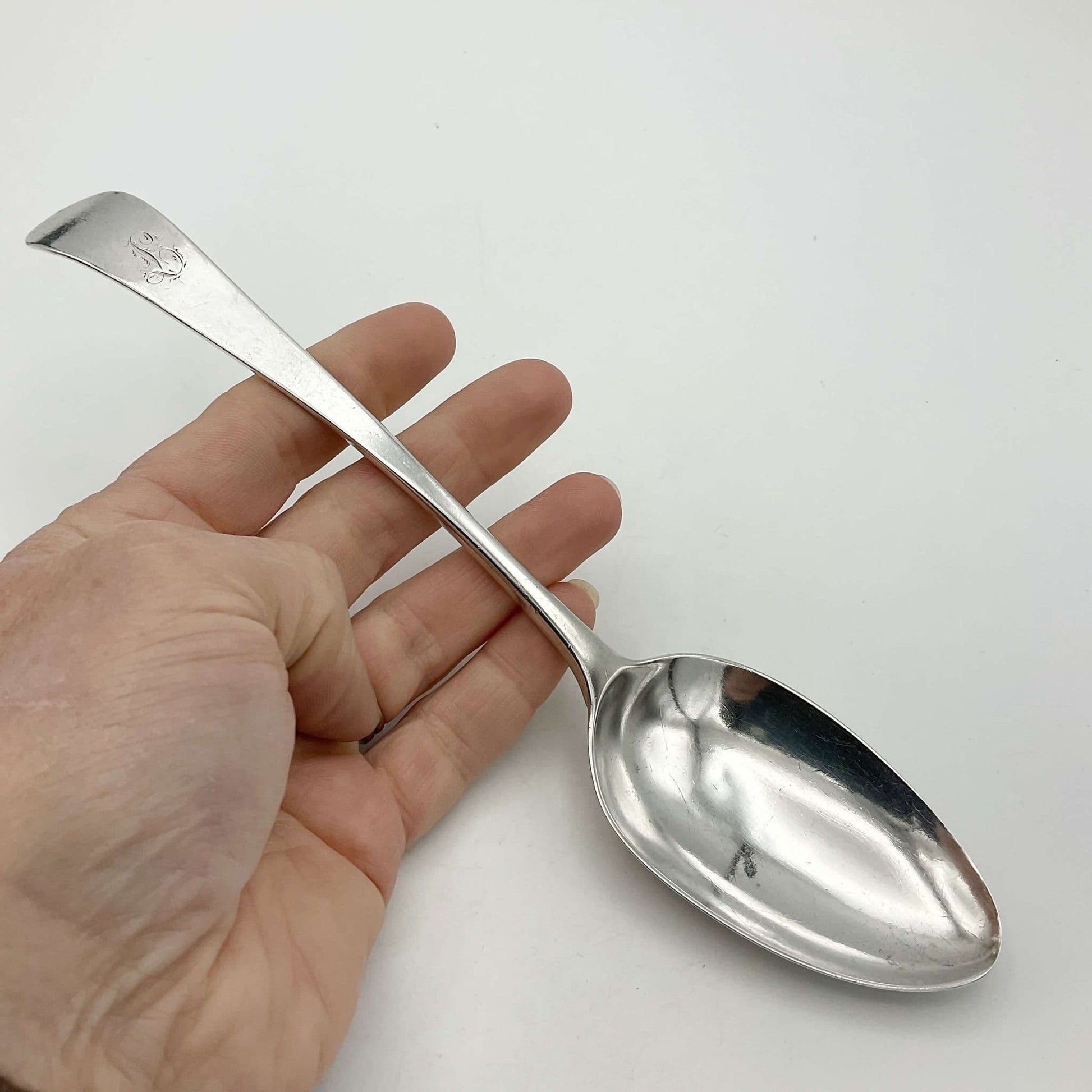 Antique silver serving spoonon held in a hand on a white background