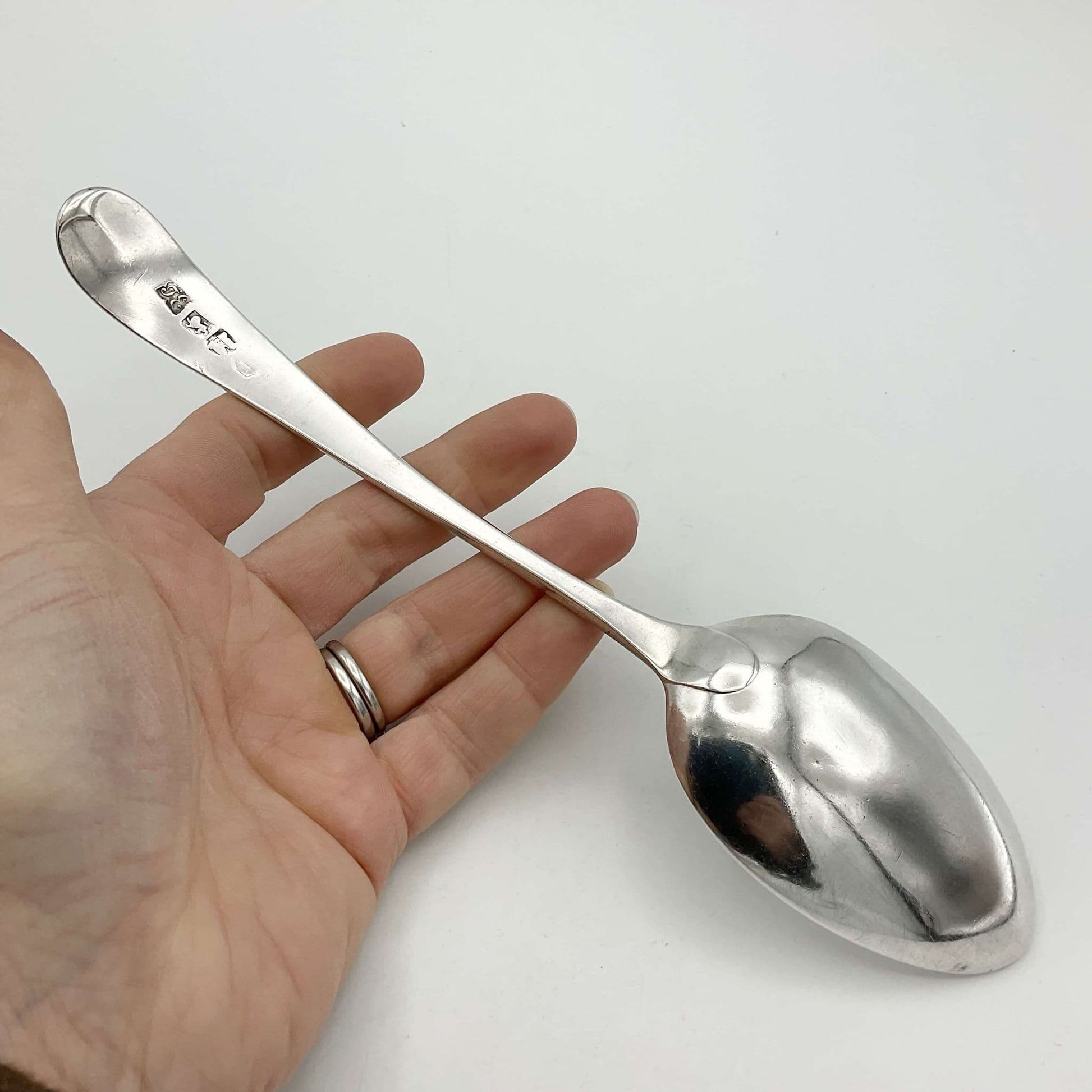 back of a Antique silver serving spoon held in a hand on a white background