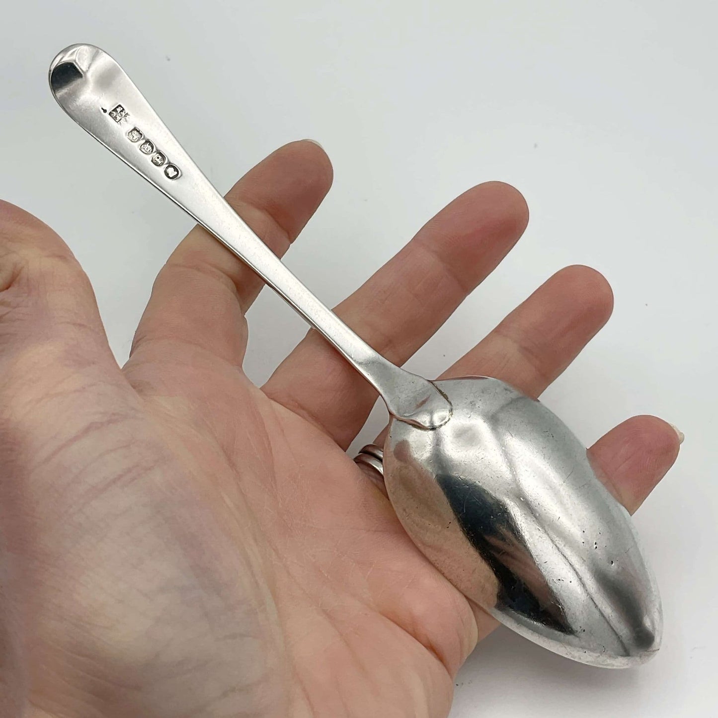 back view of Antique Georgian Sterlnig Silver Dessert Spoon on a white background held in a hand