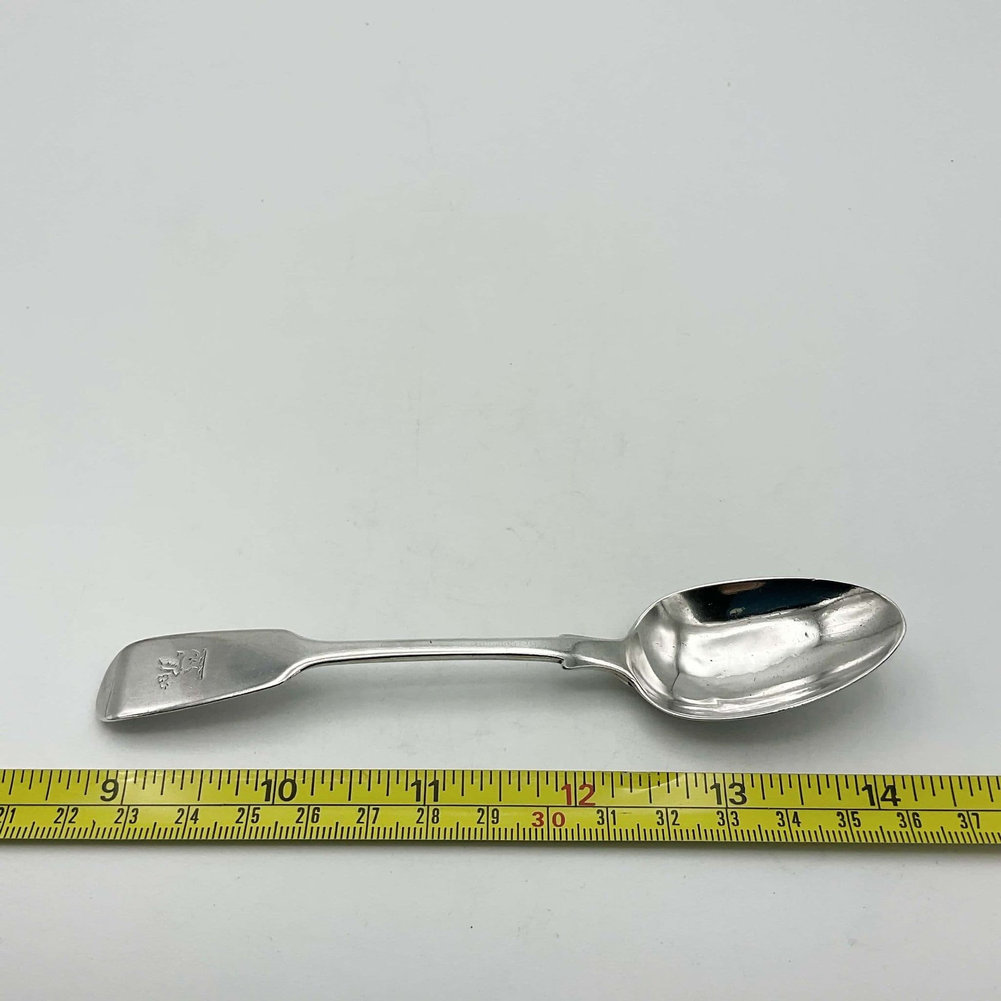 Antique silver teaspoon next to a tape measure showing it’s length as 14cm