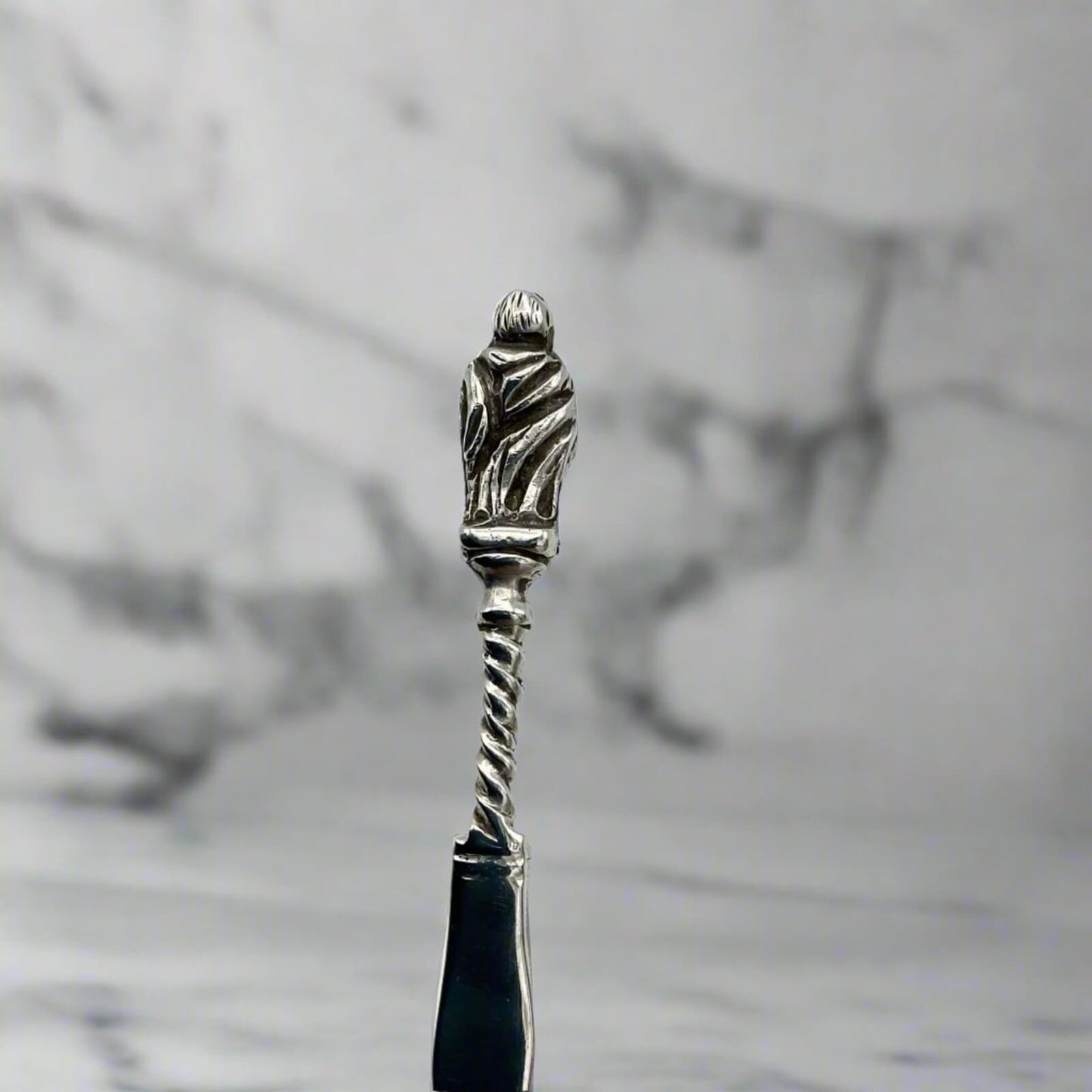 Silver-handled spoon with apostle handle on a marble background