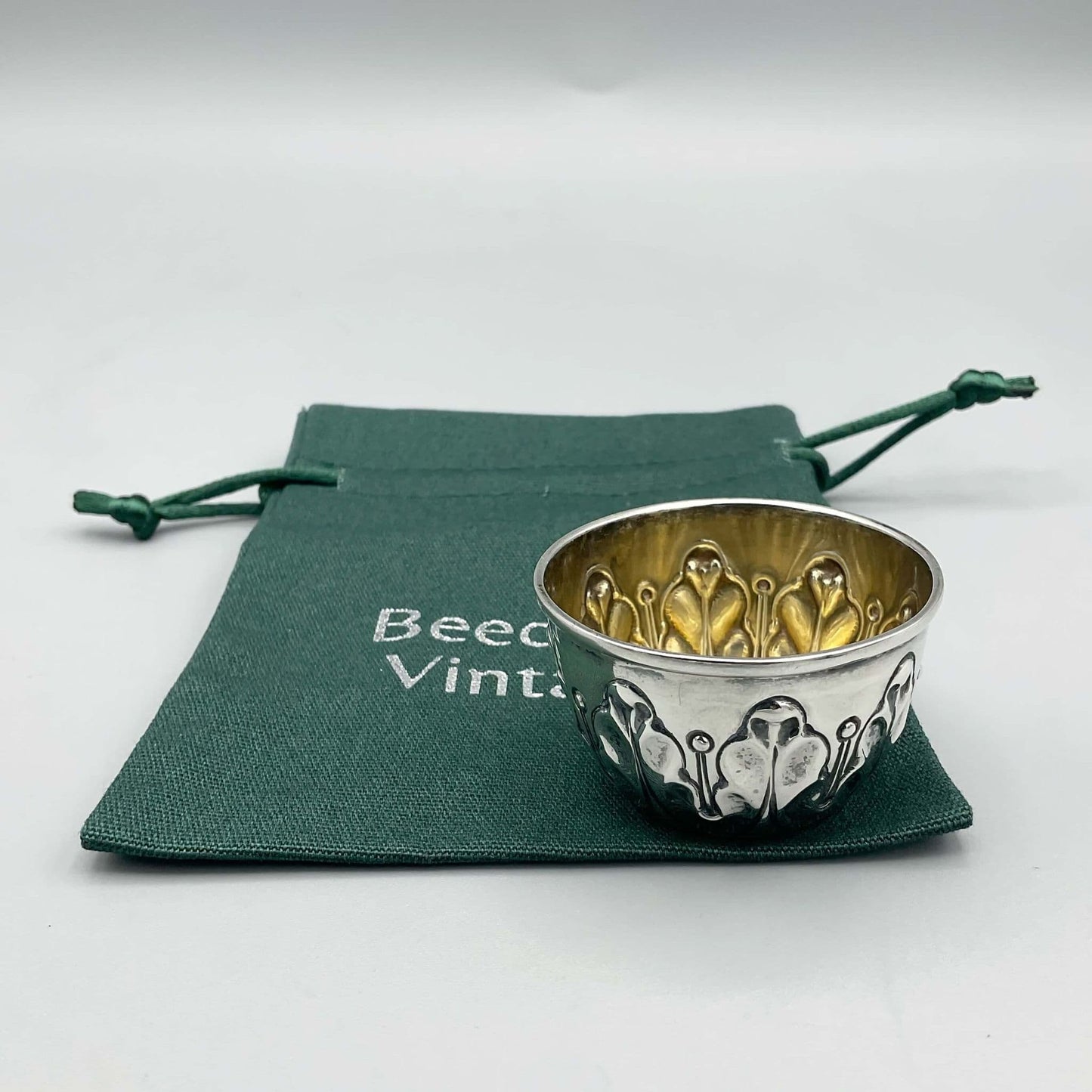 Antique Silver Salt pot with wavy design on outside and gilded interior sitting on green cotton bag