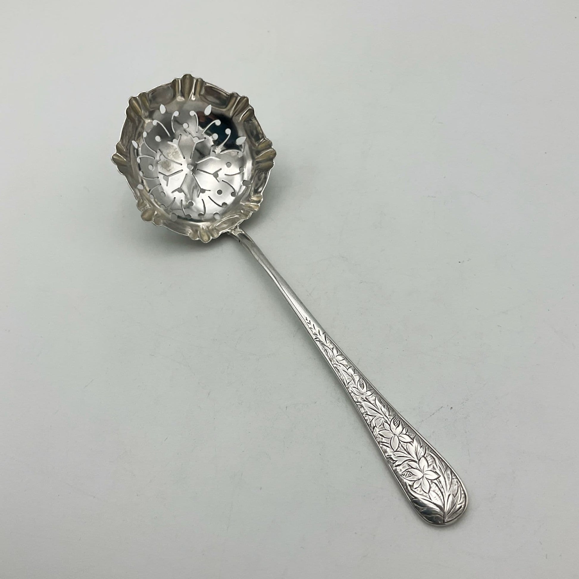 Silver sugar sifter spoon with sugar crystals on a wooden surface