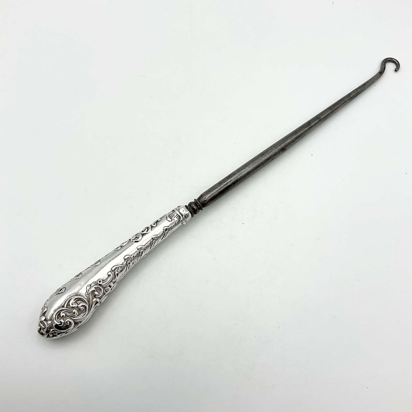 Silver handled antique button hook on a white background
