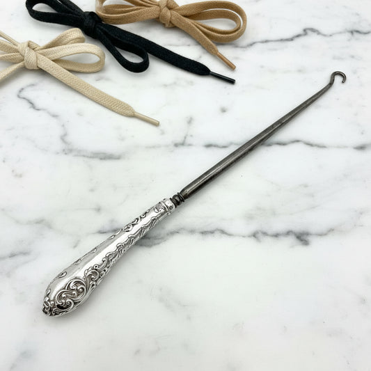 Silver handled antique button hook on a marble background with shoe laces in background