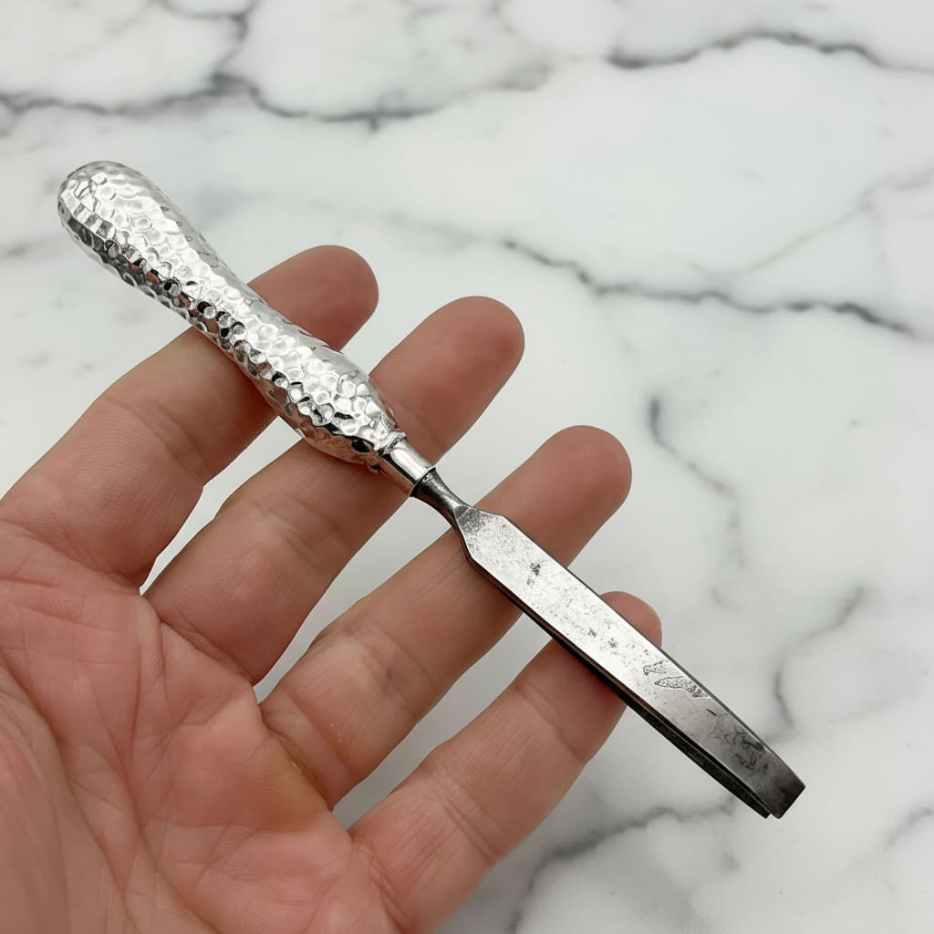 Silver tweezers with textured handle held in a hand against a marble background