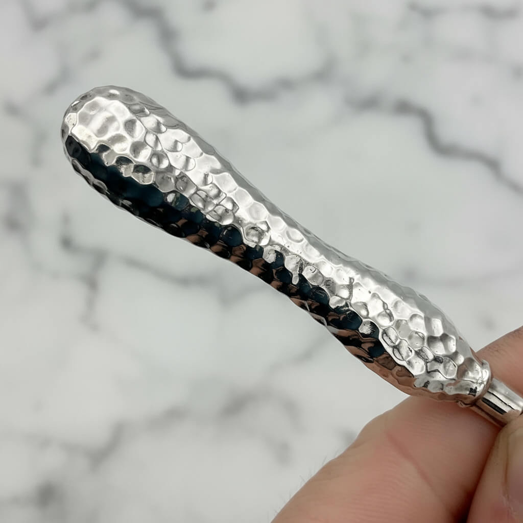 Silver textured handle tweezers held by a hand against a marble background