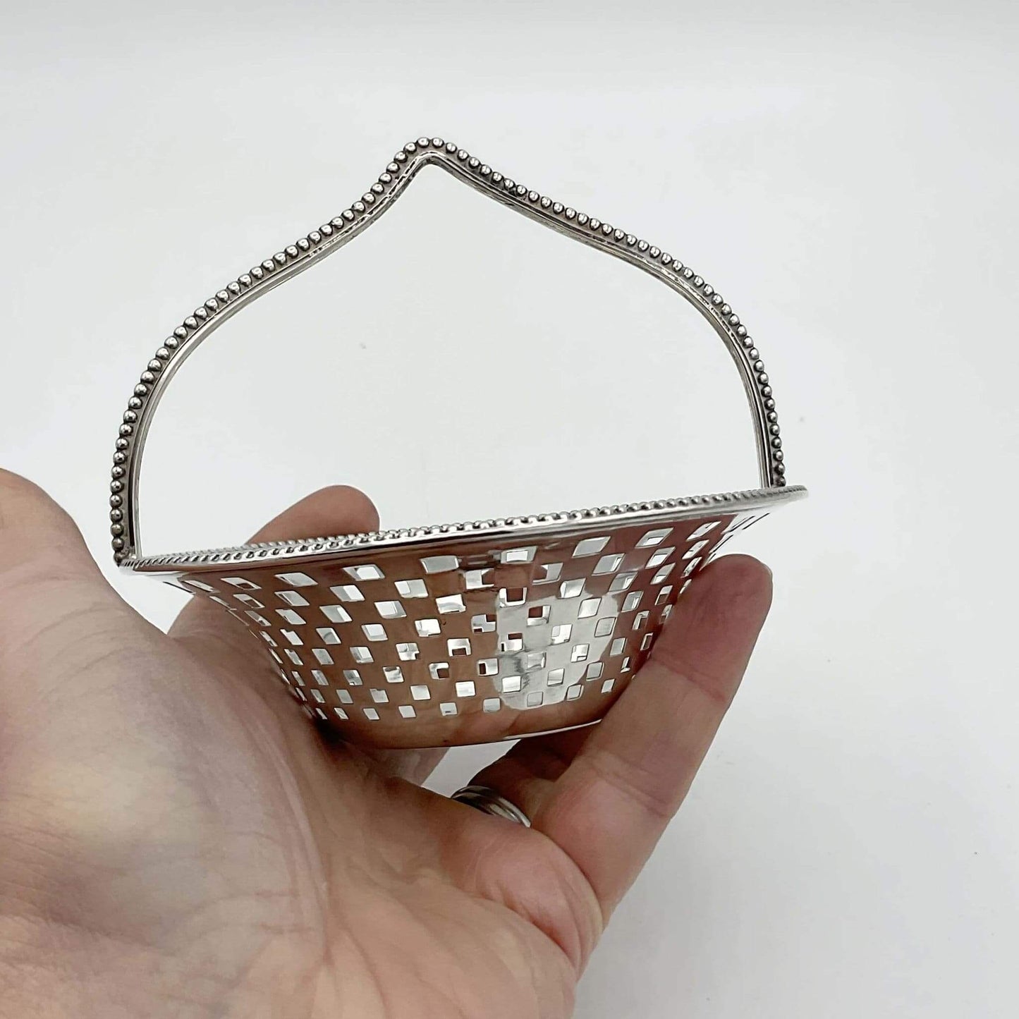 Hand holding a decorative silver basket with a checkered pattern on a white background