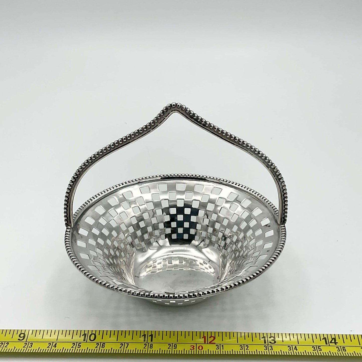 Antique Silver Basket with handle on white background next to a tape measure showing it’s 10cm in width 