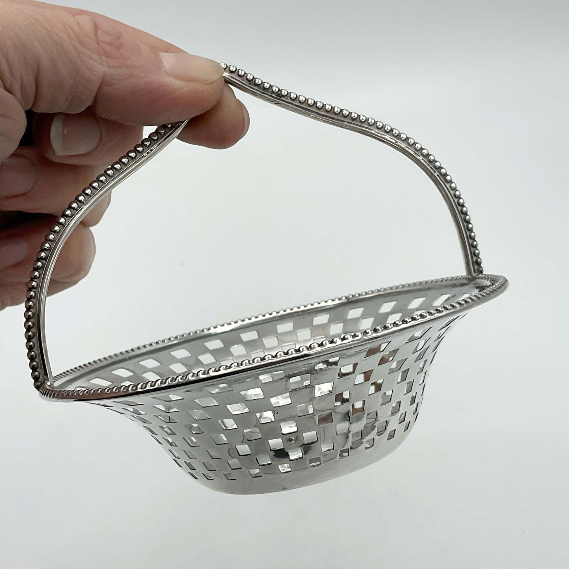 Antique Silver Basket with handle held by fingers showing pierced side on white background