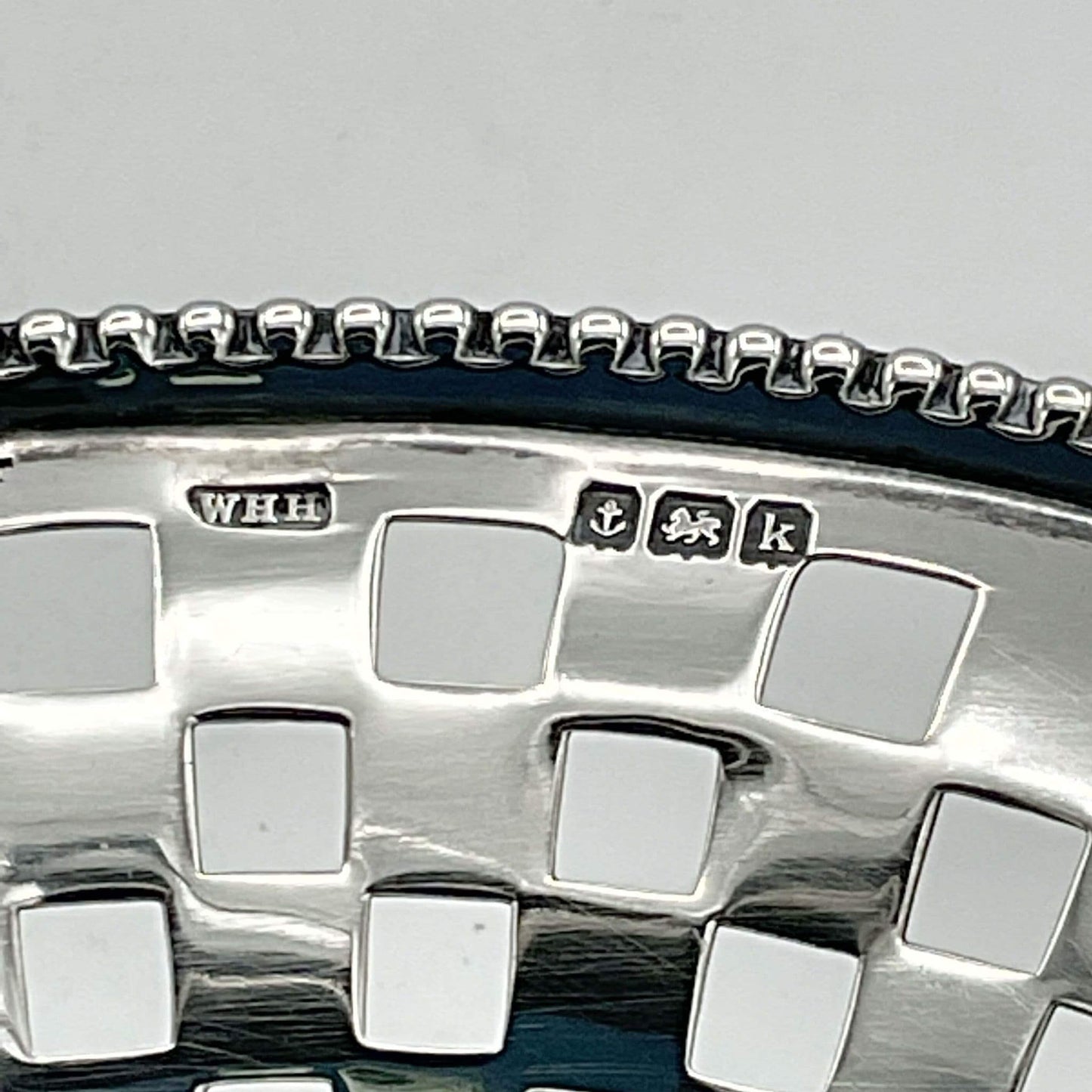 Close-up of a silver basket with engraved hallmark details on a light gray background