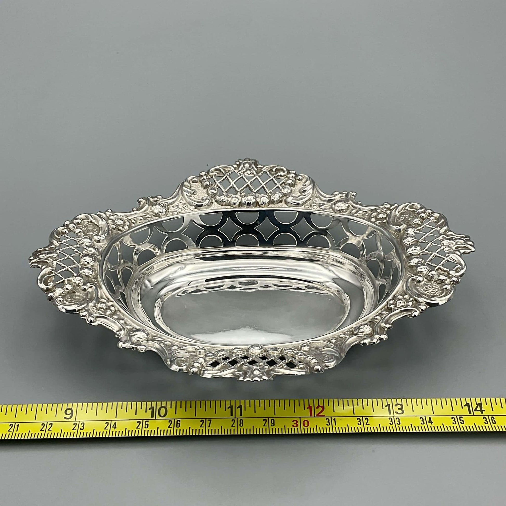 Ornate silver pierced bowl on grey background With tape measure showing size as approximately 15cm