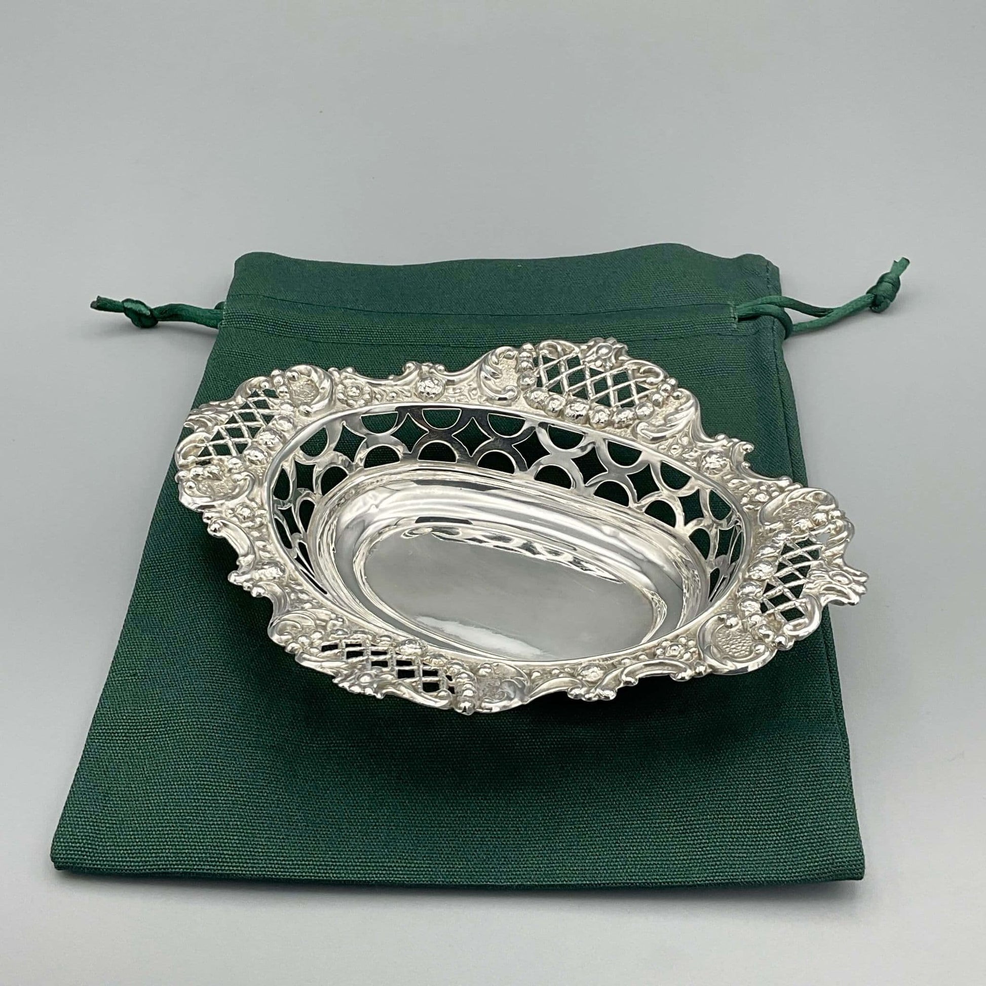 Ornate silver pierced bowl on grey background Sitting on green cotton gift bag