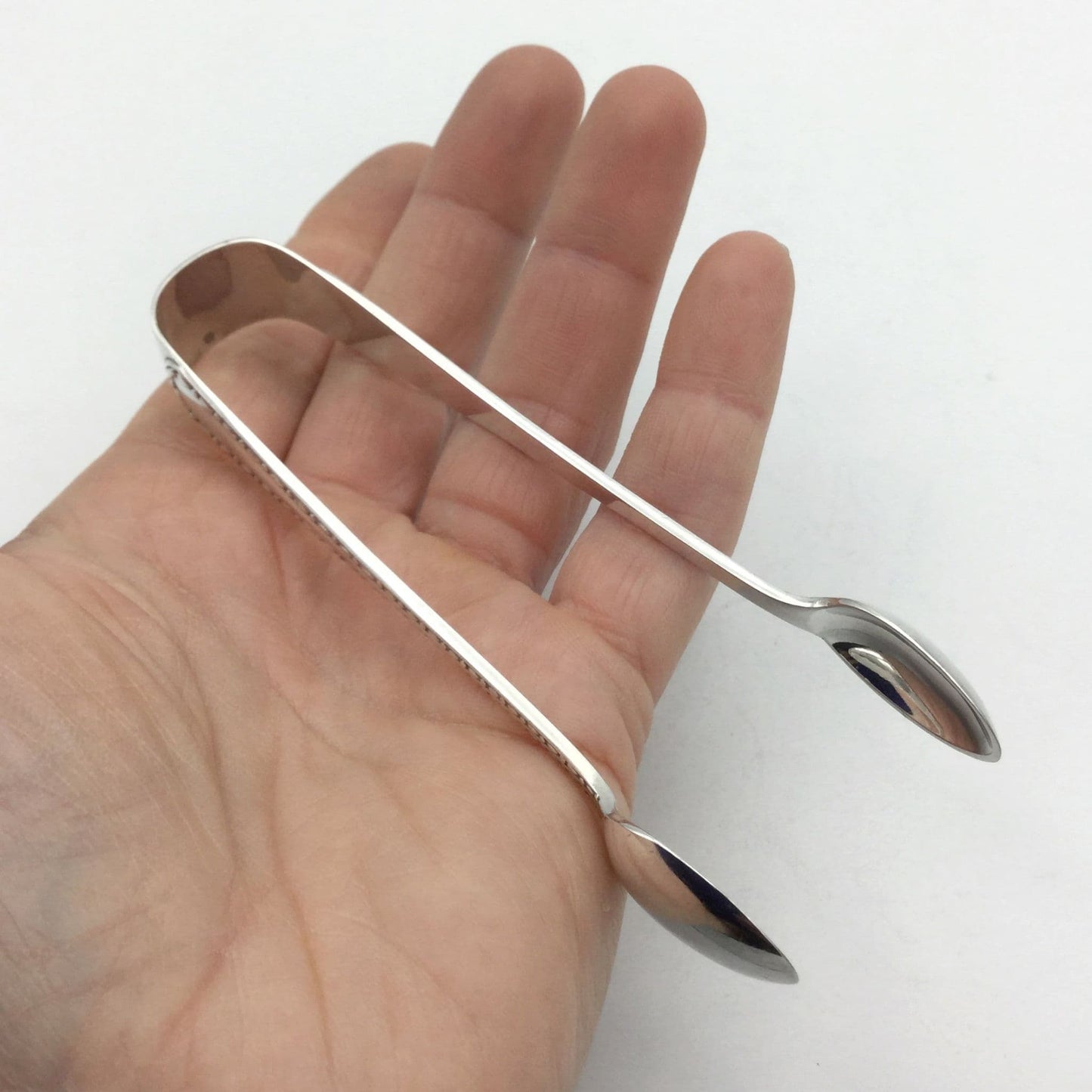 Silver plated sugar tongs in the palm of a hand
