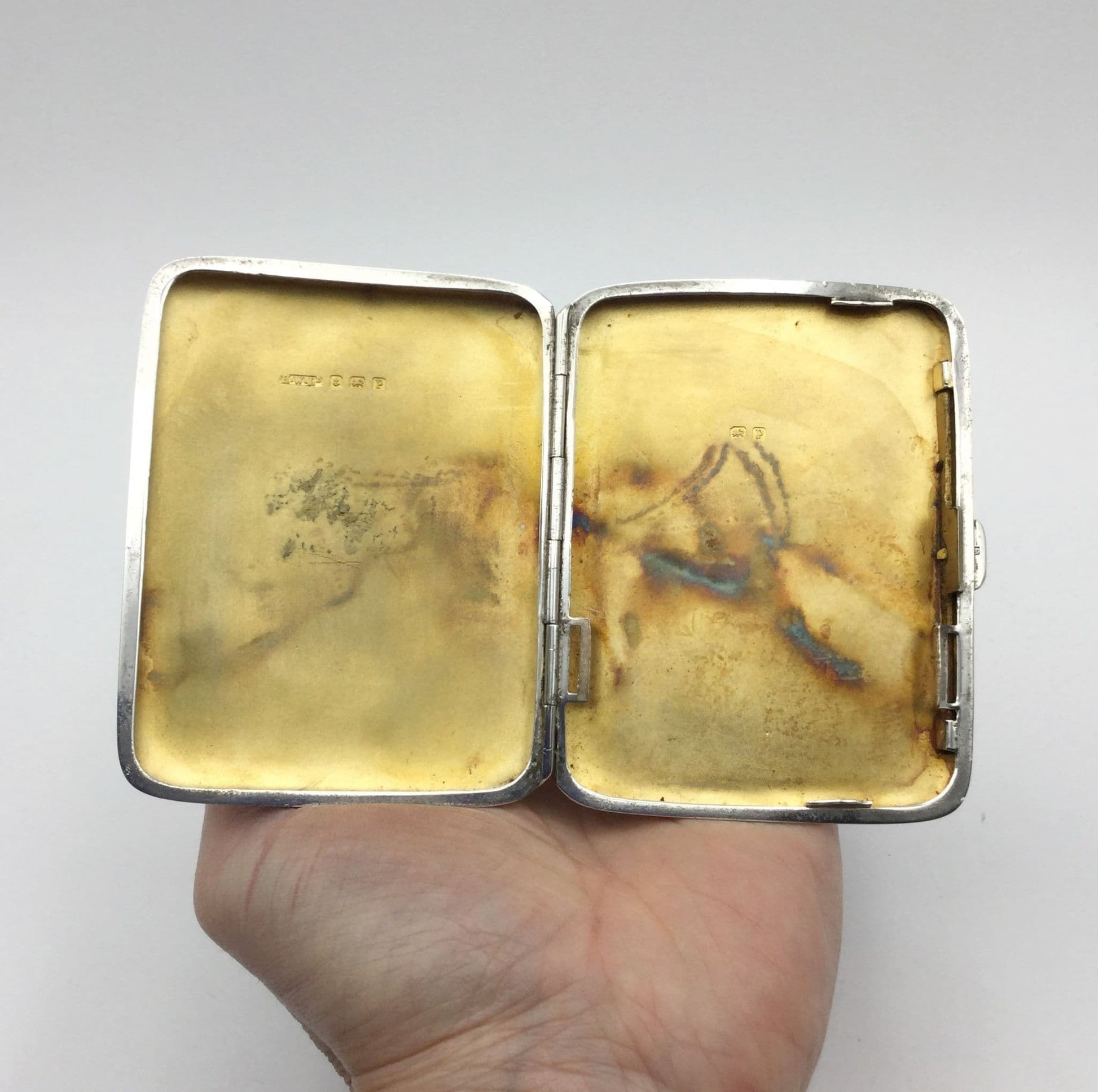 open antique silver cigarette case showing a lovely golden gilded interior held in a hand