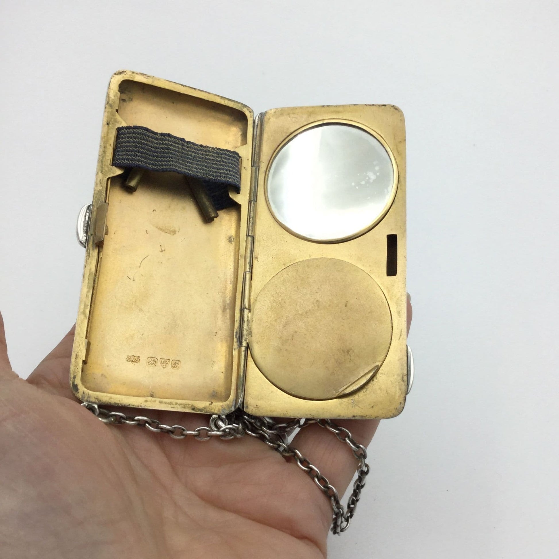 gilded golden inside of case showing a mirror, powder area and chain held in a hand
